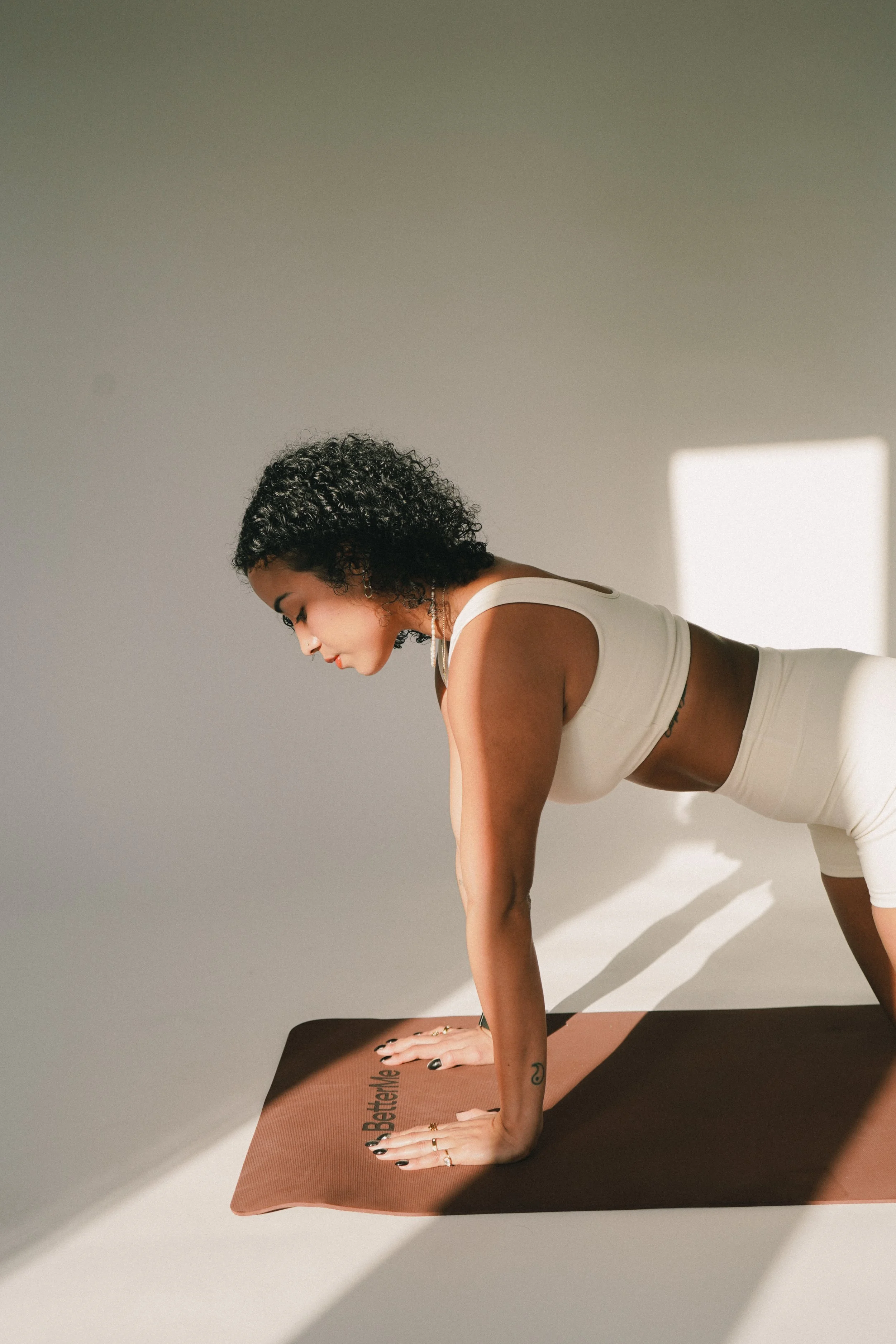A woman with curly hair practicing yoga on a brown mat in a well-lit room.