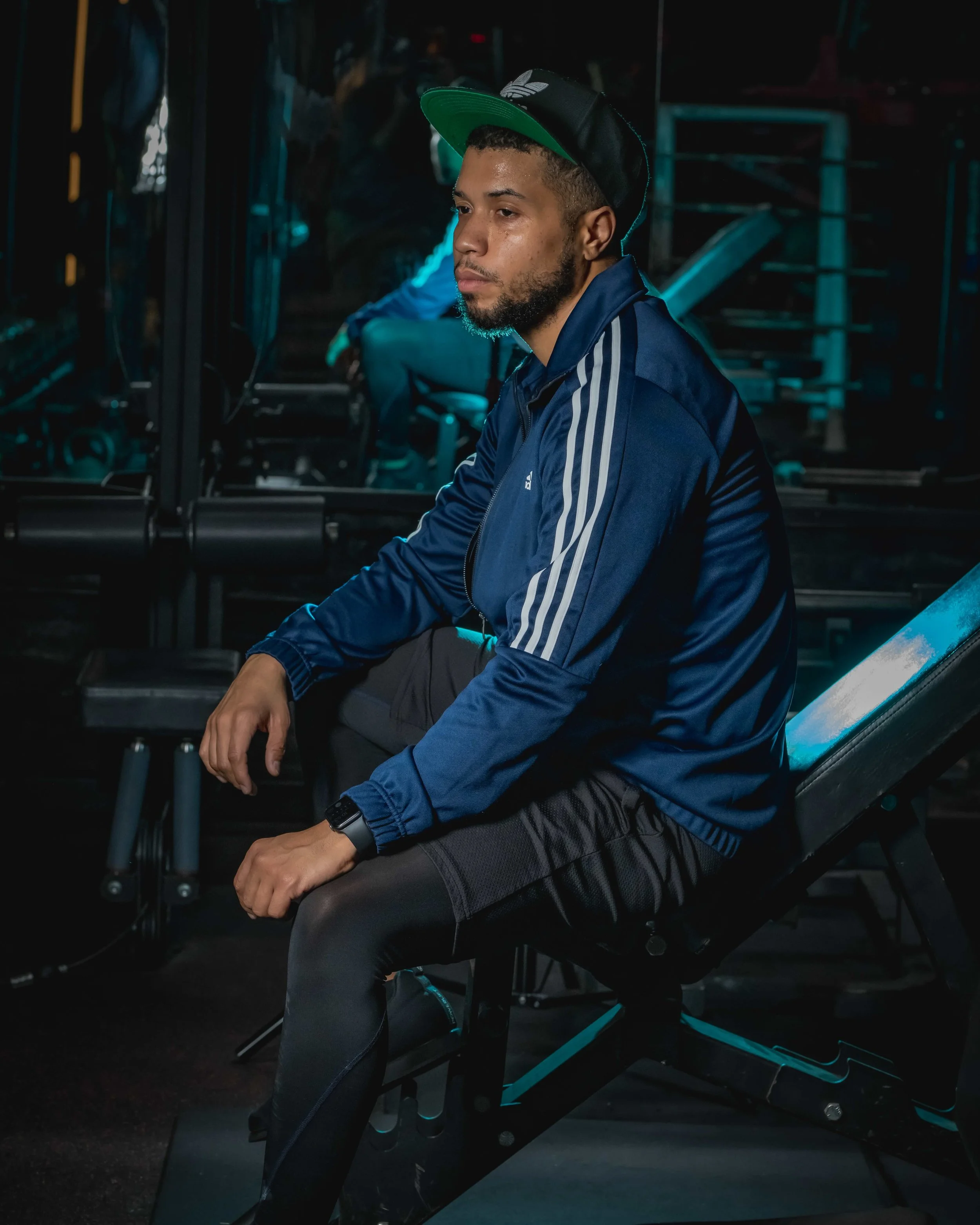 Man sitting on gym workout bench in gym with dark lighting