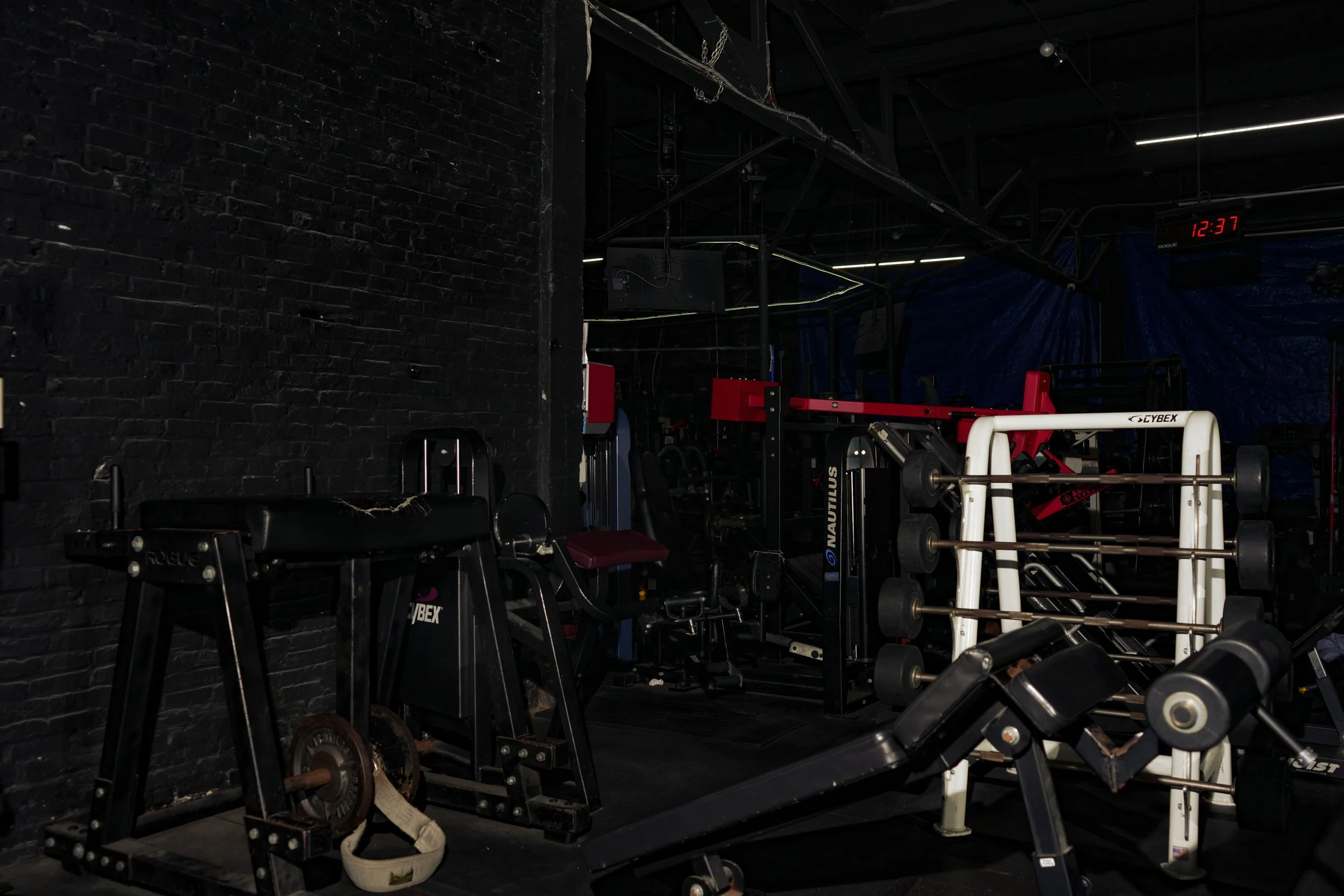 Empty gym with black brick wall and various workout equipment including a weight bench, barbells, and weight plates.
