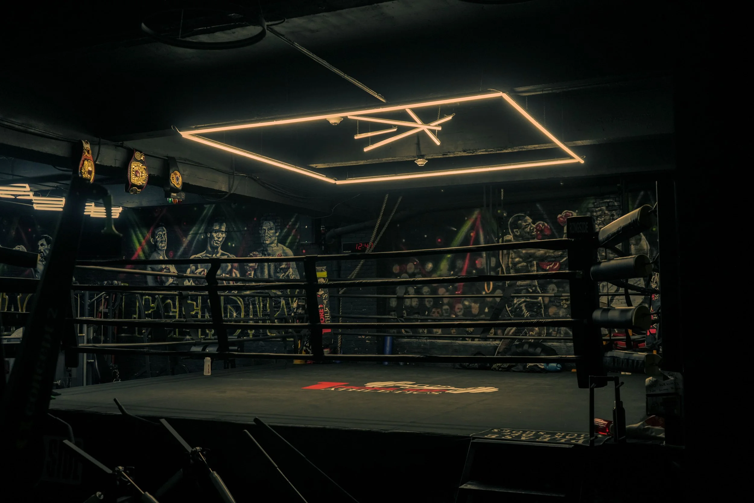Empty boxing ring inside a gym with graffiti murals on the wall.