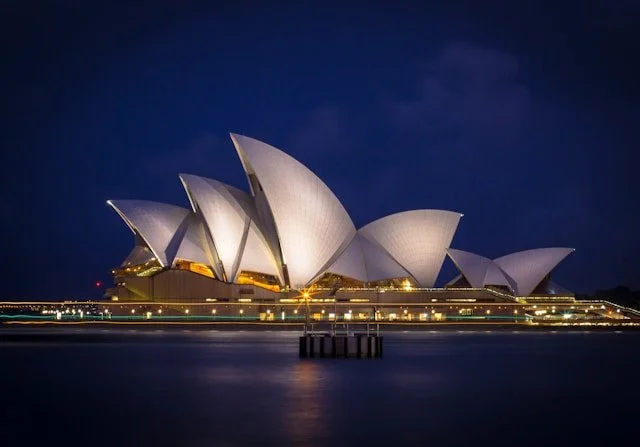 Sydney Opera House illuminated at night, reflecting on the water.