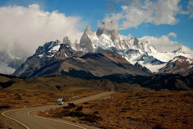 Winding road leading toward snow-capped mountains under a partly cloudy sky.