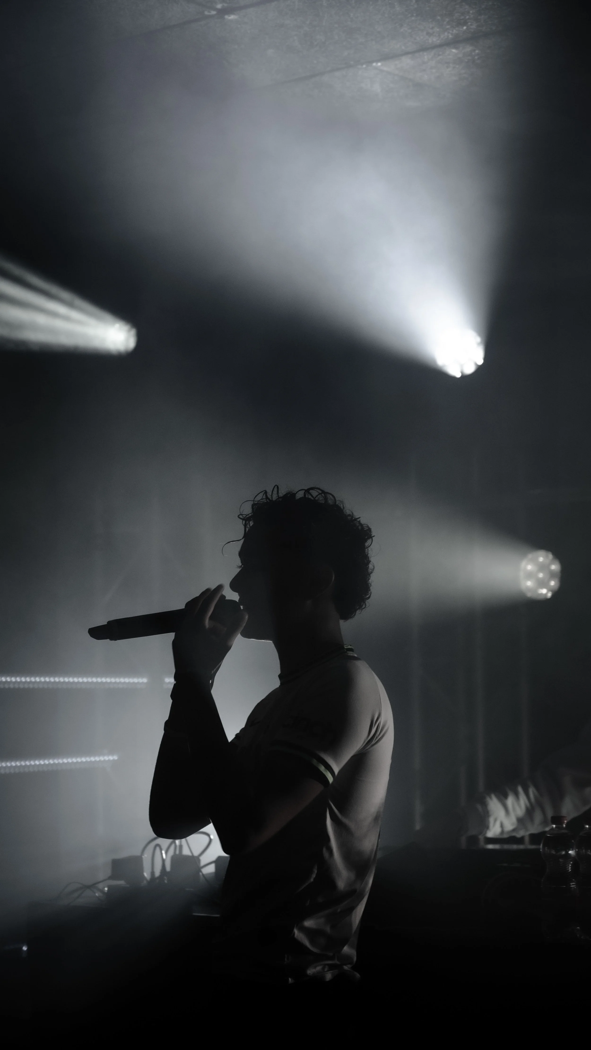 Une silhouette d'une personne qui chante avec un microphone dans un environnement sombre et brumeux, avec des effets de lumière sophistiqués.