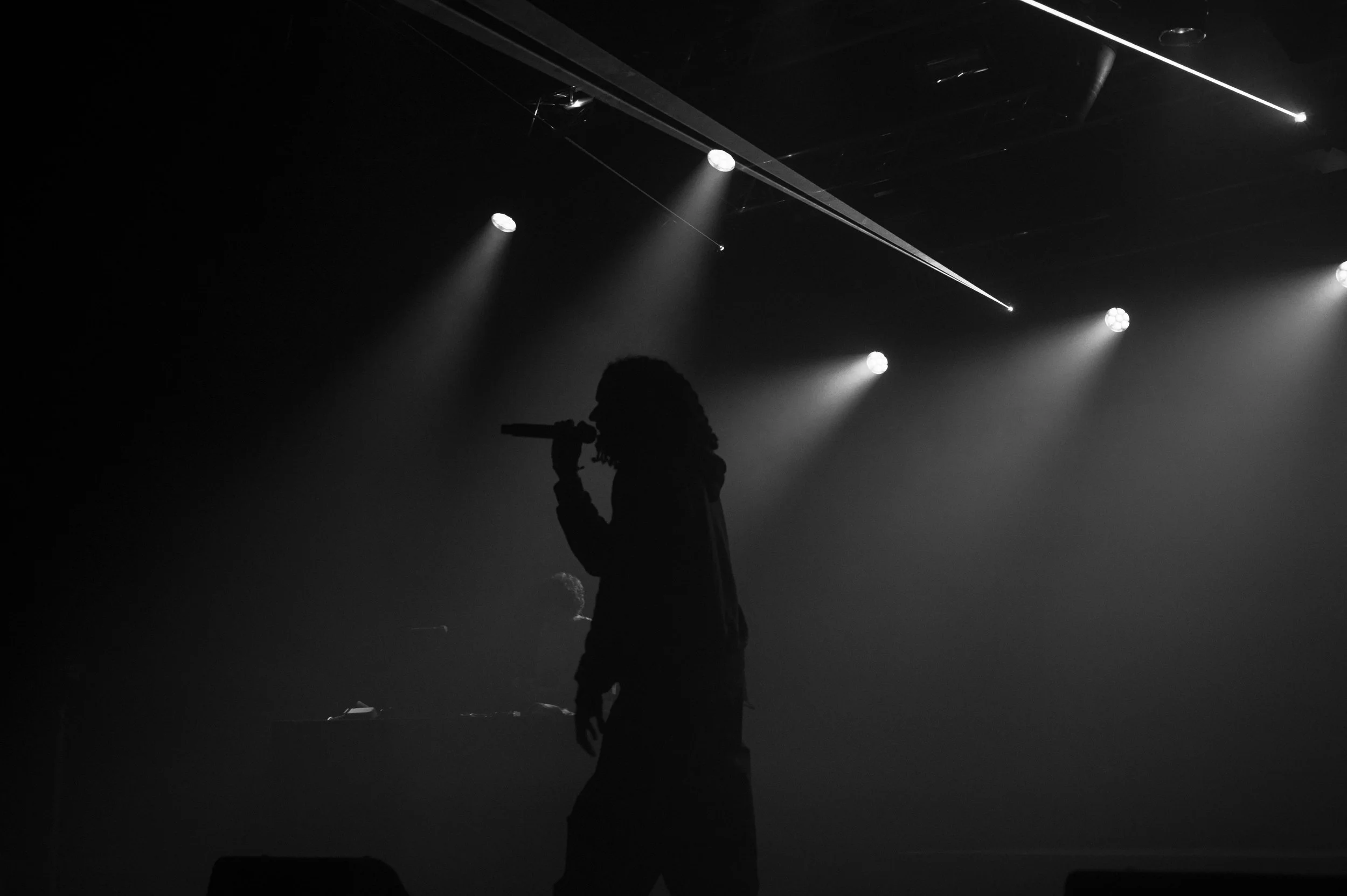 Silhouette d'une personne avec un microphone sur scène, éclairée par des projecteurs, avec un fond sombre.