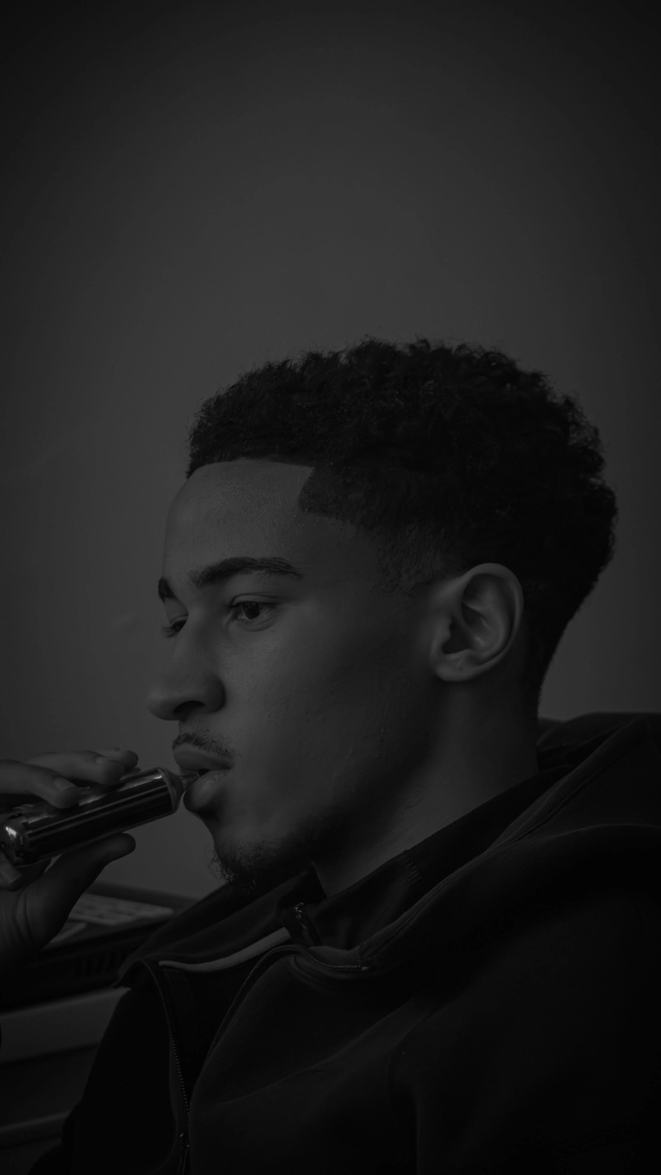 Un jeune homme noir avec des cheveux bouclés courts joue de la flûte, en noir et blanc.