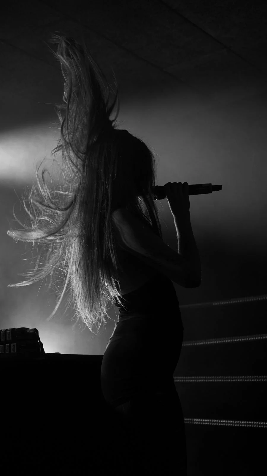 Silhouette d'une femme chantant dans un microphone, cheveux en mouvement, en noir et blanc.