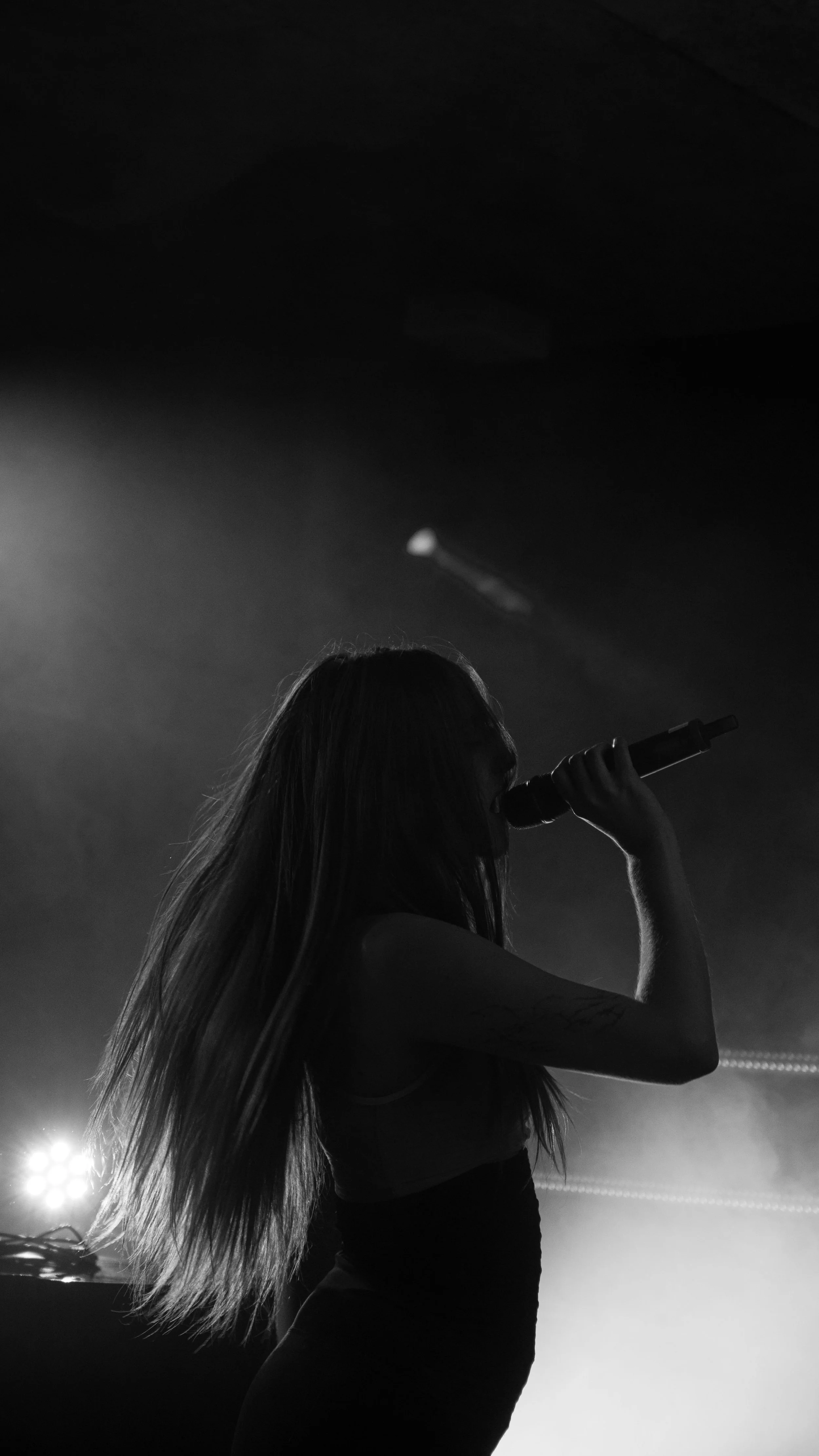 Une femme essayant de chanter ou de parler dans un microphone, dans une scène sombre avec un éclairage dramatique.