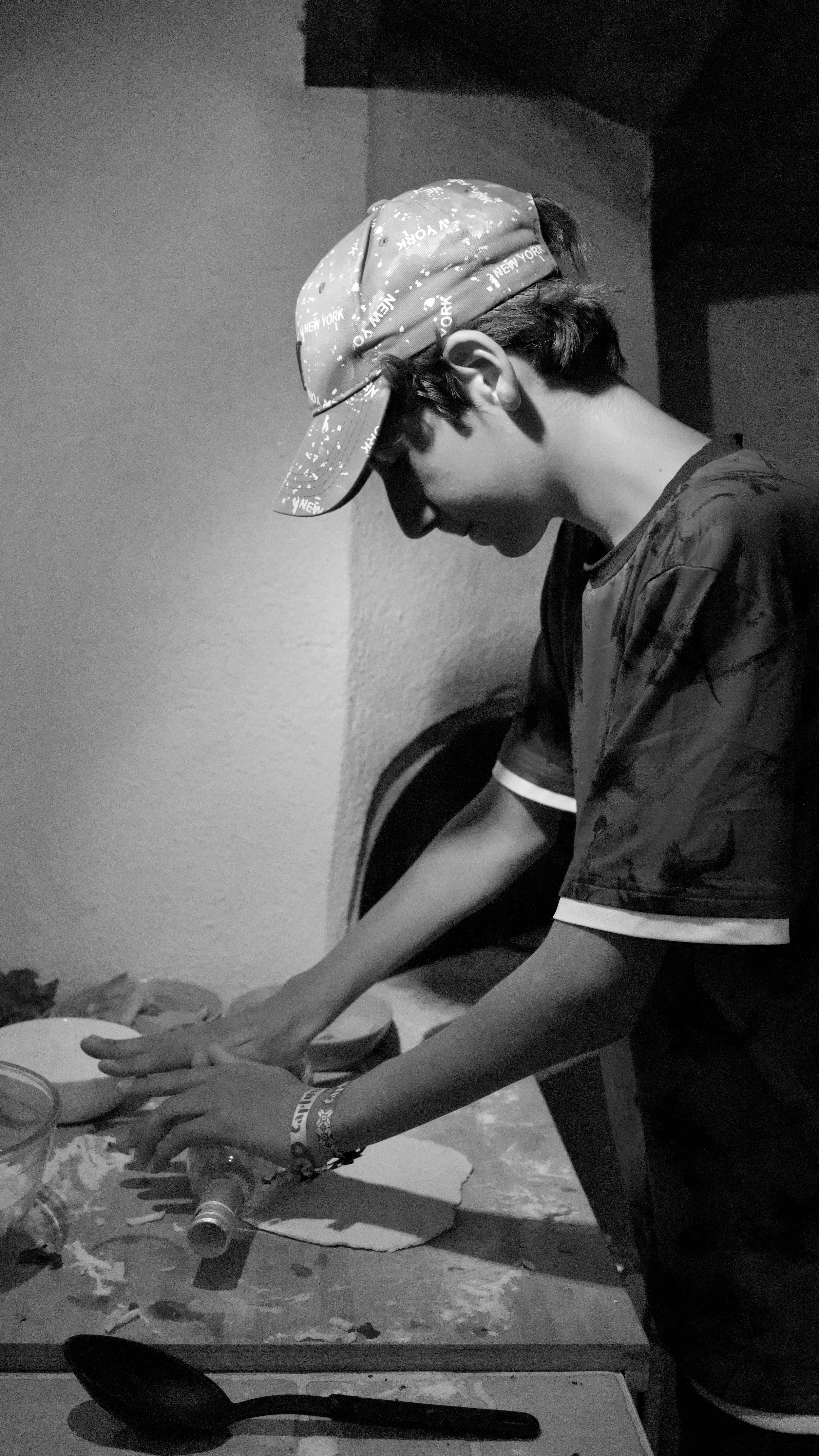 Une personne portant une casquette, en train de couper quelque chose sur une table dans une pièce sombre.