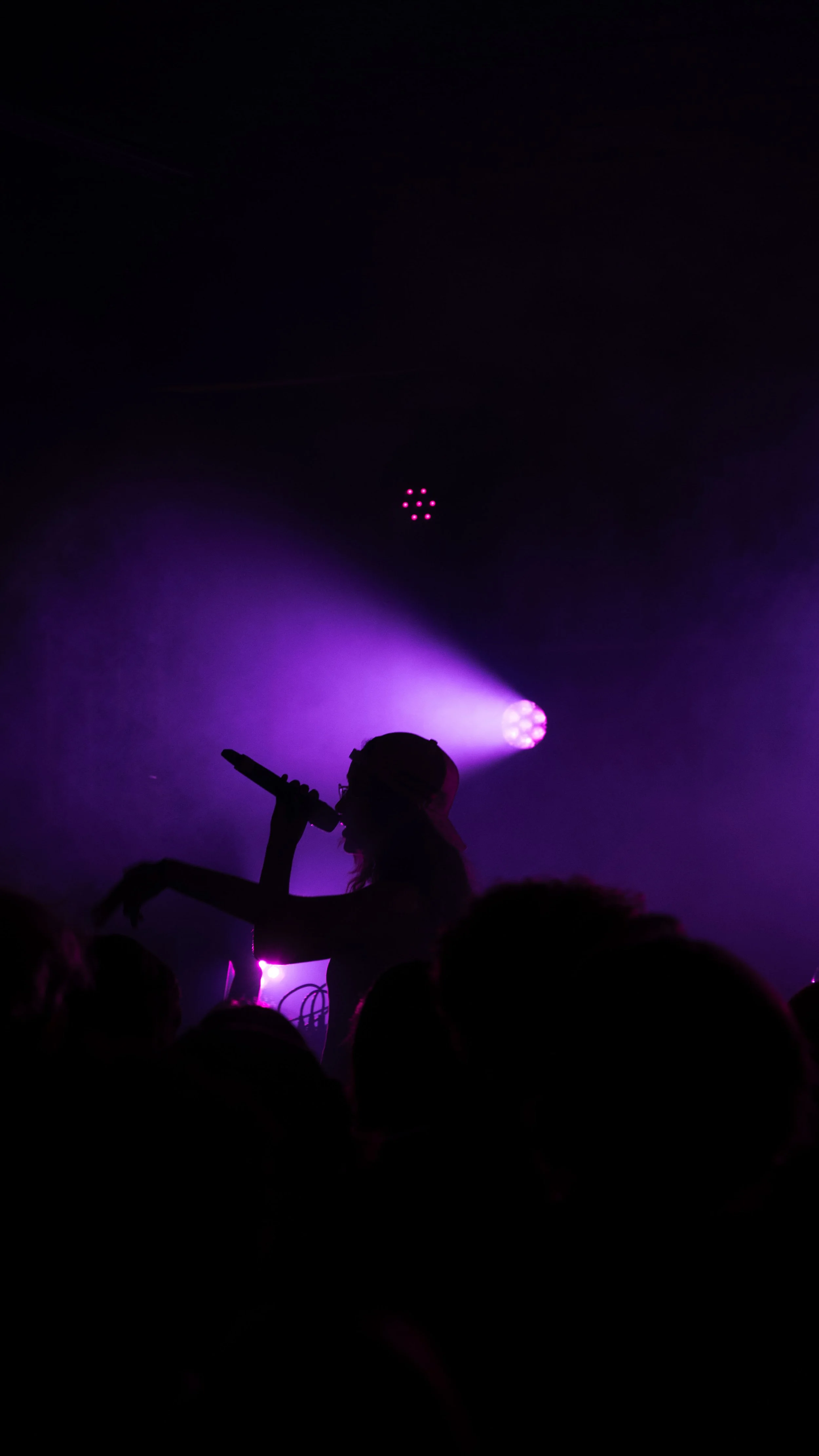 Silhouette d'une personne chantant dans un micro avec des lumières violettes sur scène, dans une foule.