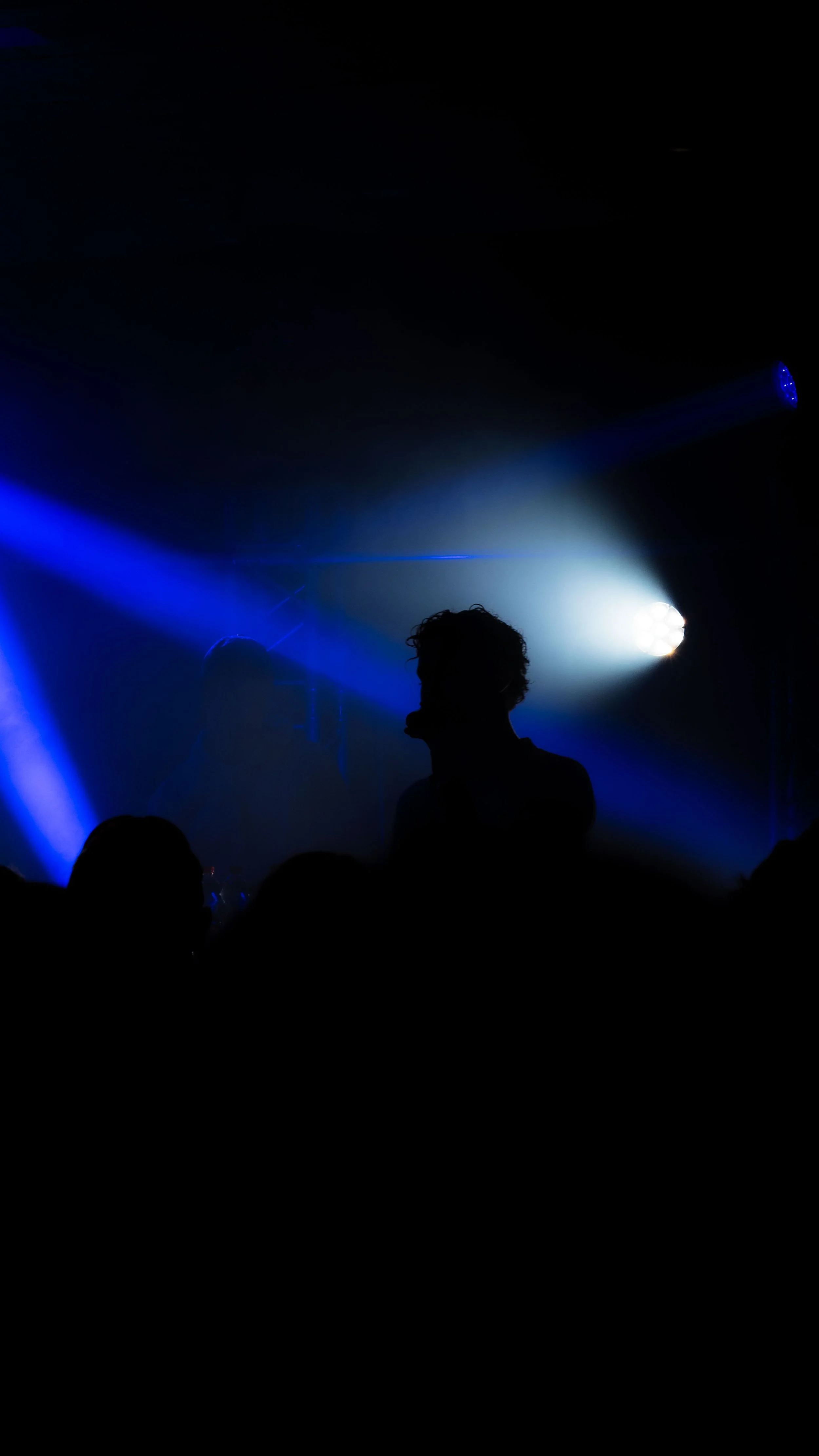 Silhouettes de personnes dans un espace sombre avec des lumières bleues et blanches, ambiance de scène ou de concert.
