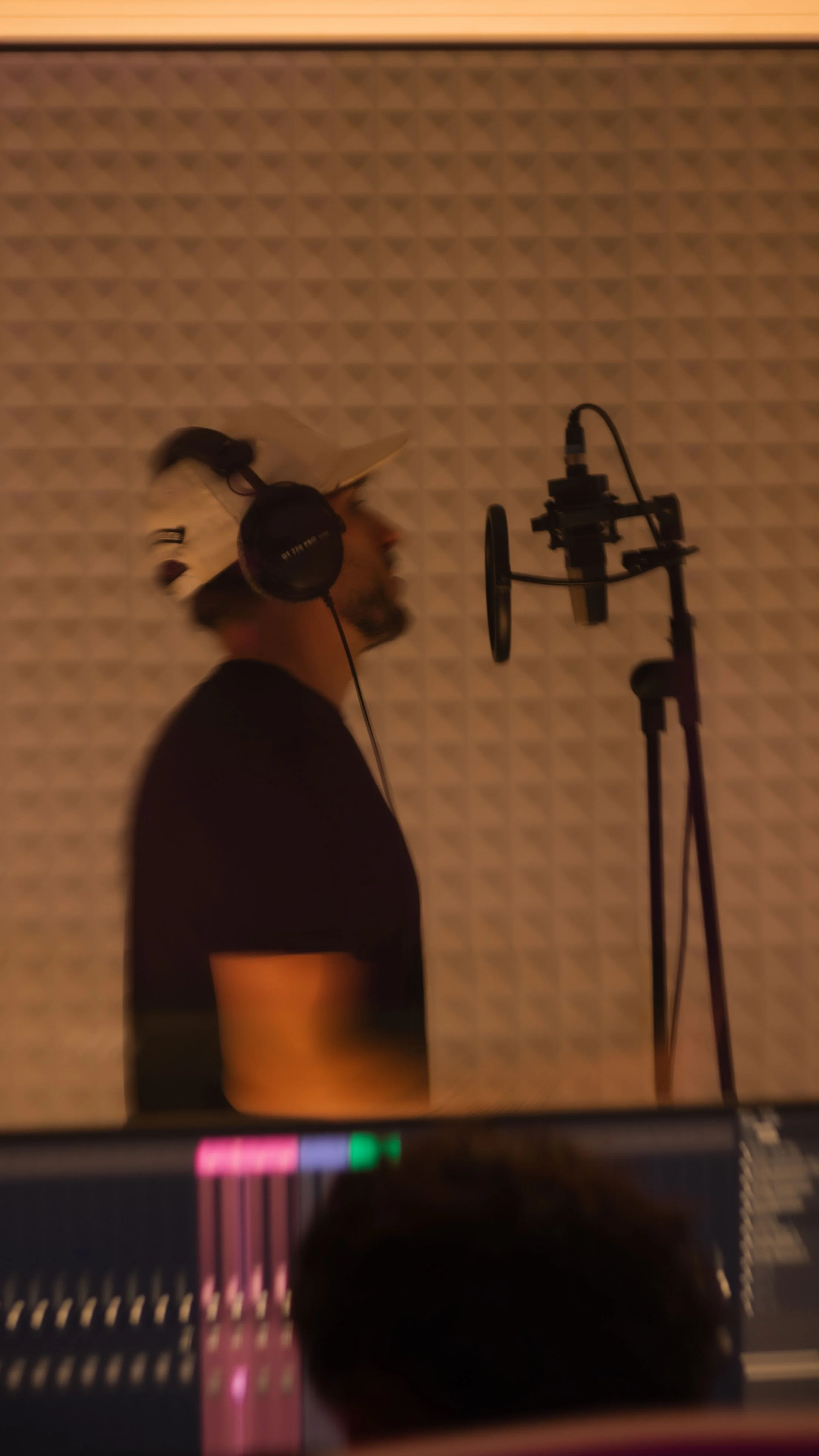 Un homme portant un casque d'écoute en studio d'enregistrement, devant un microphone, avec un mur revêtu de panneaux acoustiques.