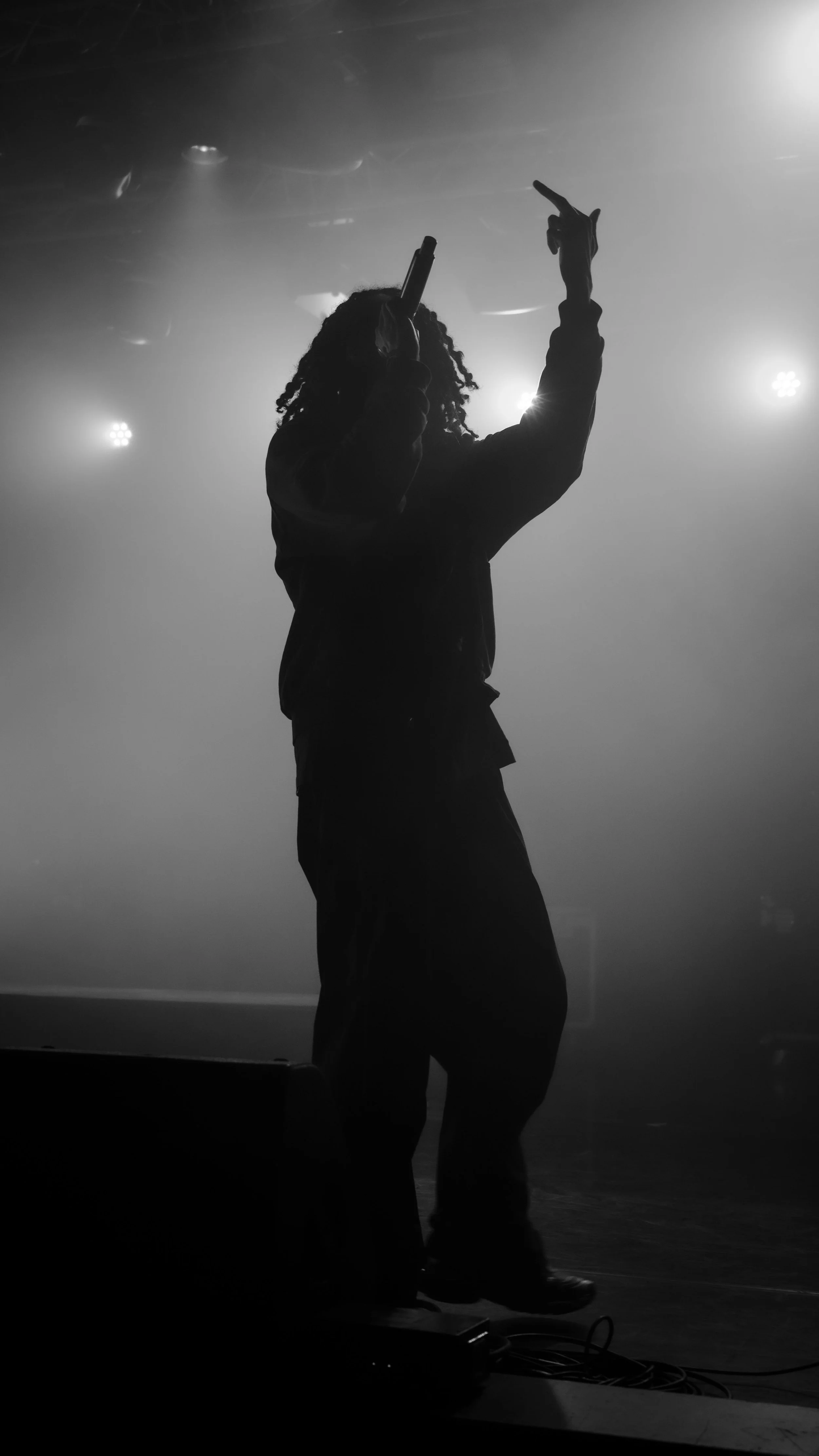 Silhouette d'une personne avec un micro, en train de chanter ou de performer sur scène sous un éclairage fort, ambiance sombre.