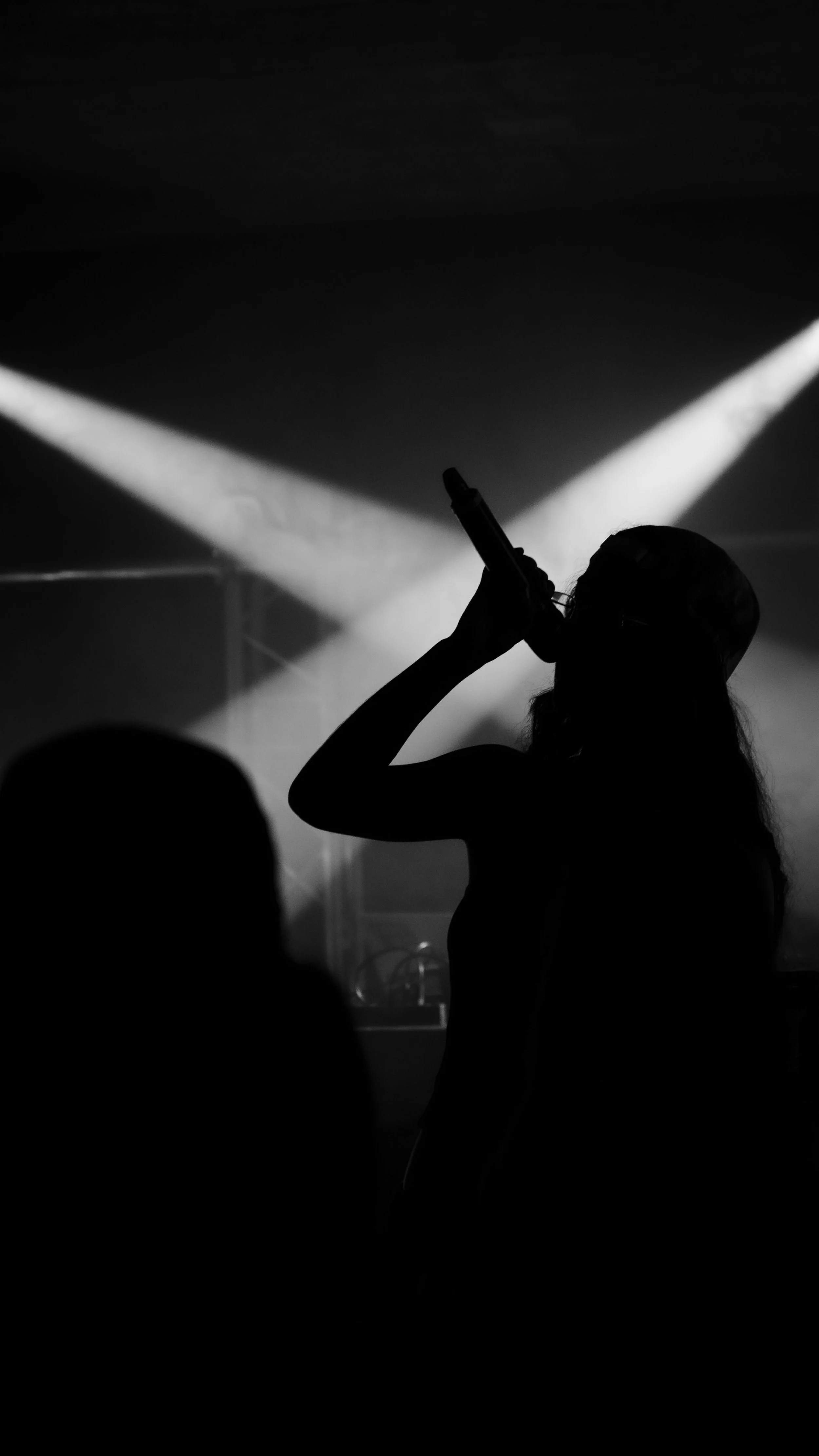 Silhouette d'une personne tenant un microphone dans une scène sombre avec des lumières en arrière-plan.