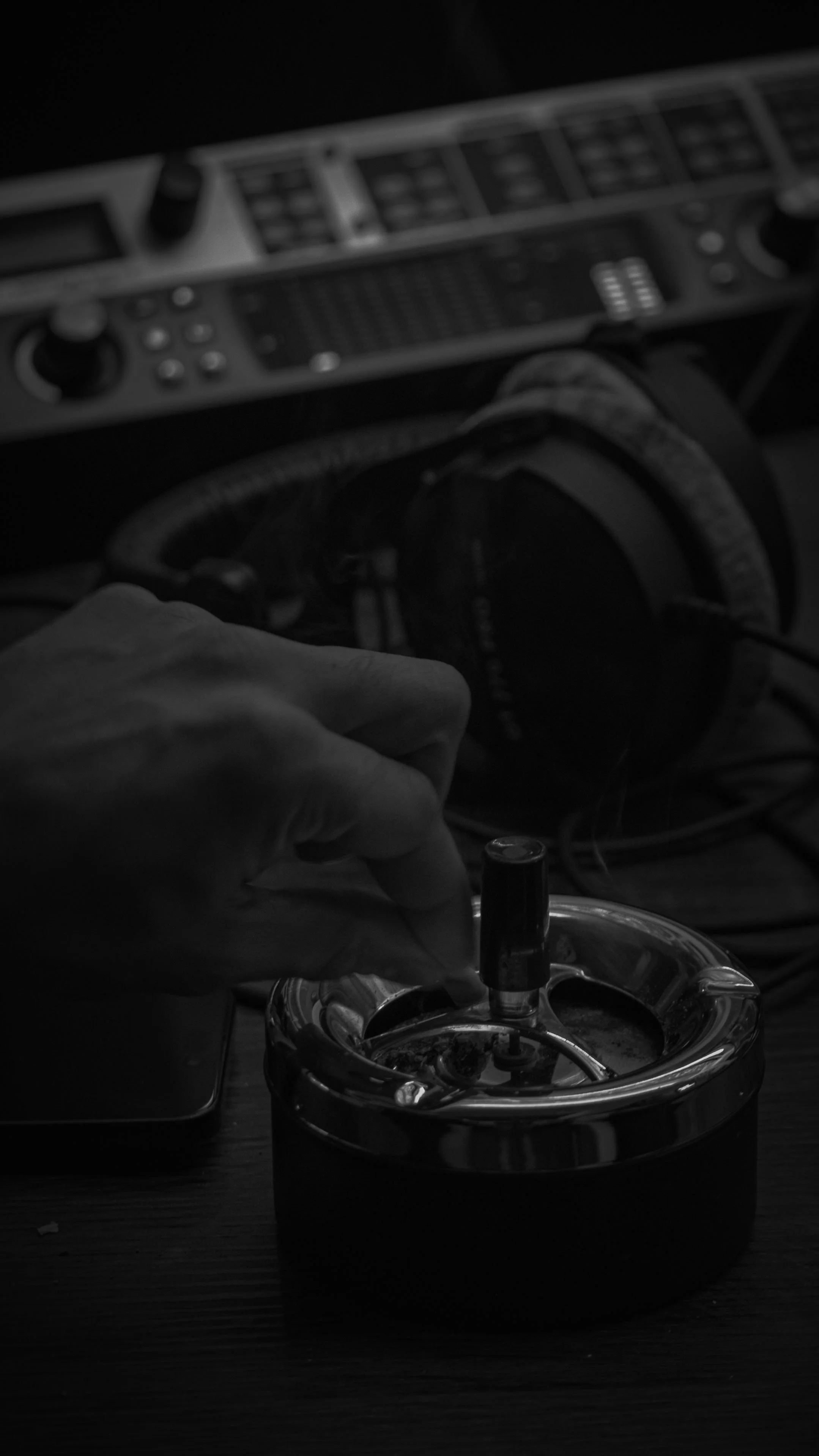 Une main qui manipule un objet dans un réservoir placé sur une surface en bois, avec un équipement audio ou DJ en arrière-plan.