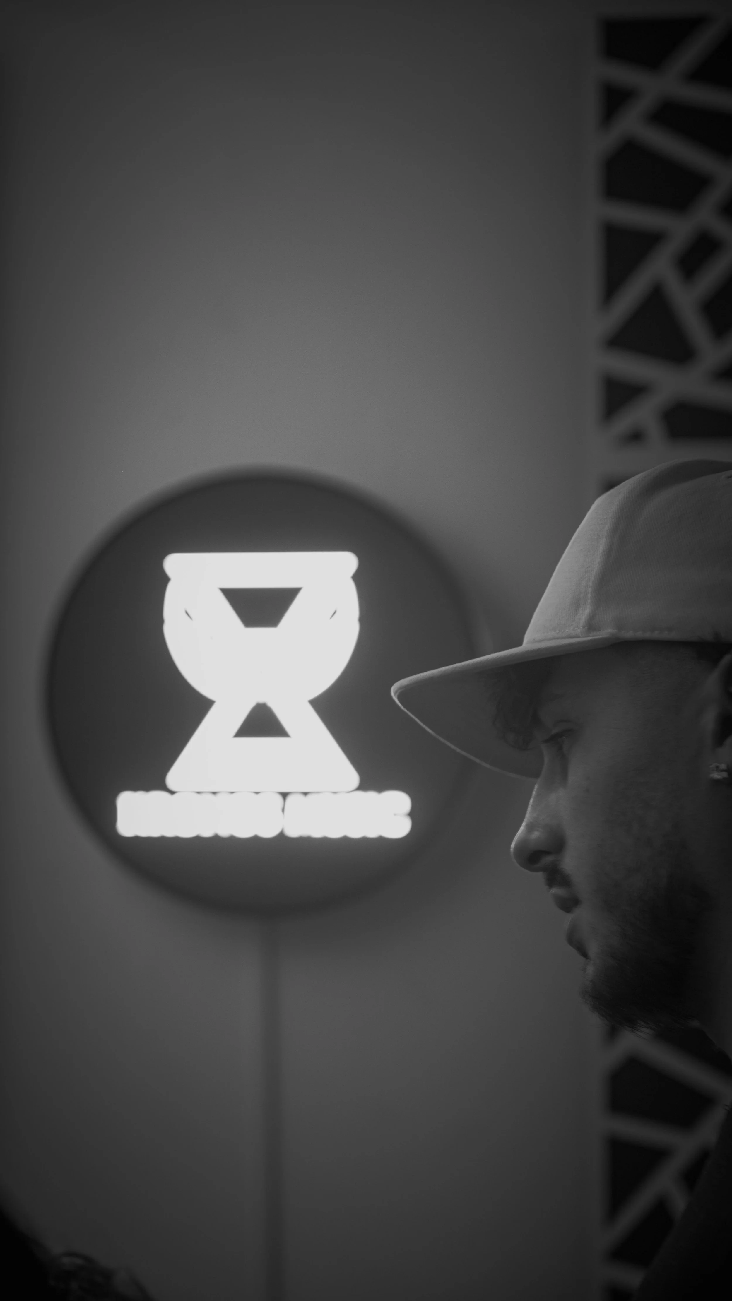 Une femme portant un chapeau regarde vers la droite, avec un fond de panneau lumineux affichant un logo en forme de coupe ou de bol avec un fond clair.