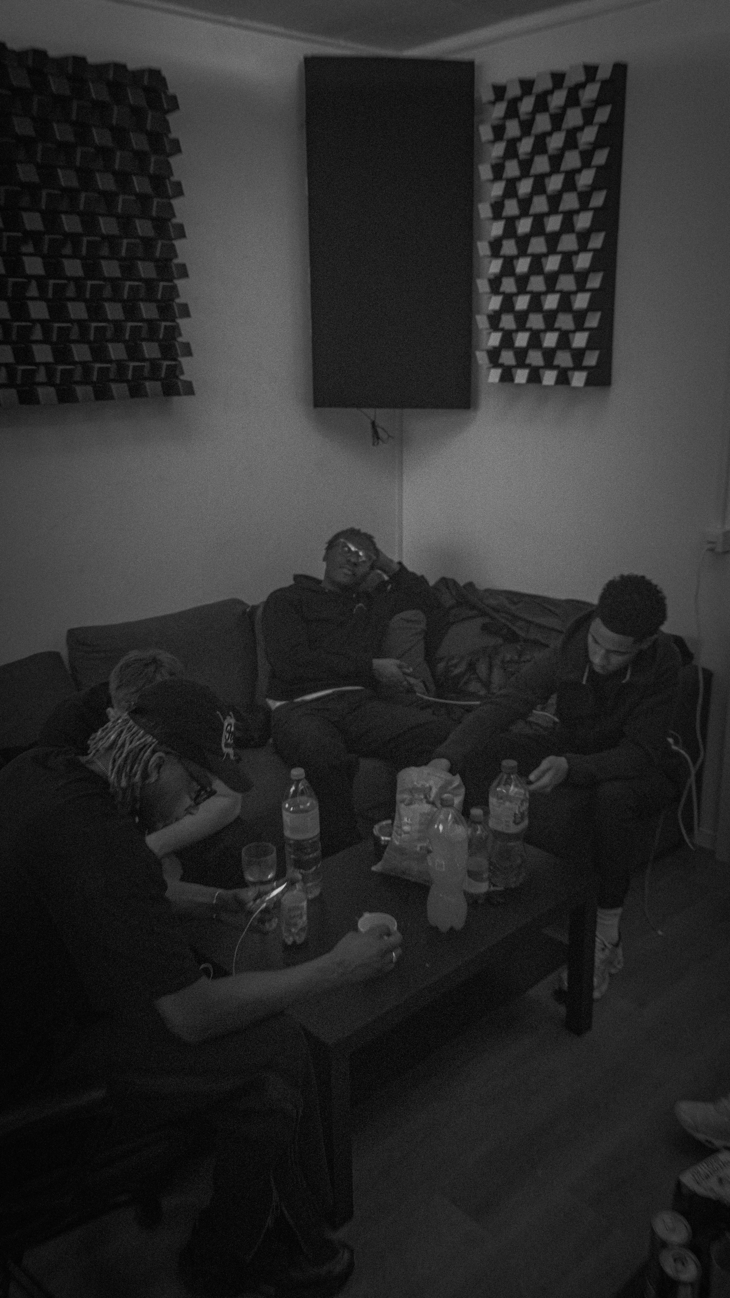 Groupe de personnes assises autour d'une table avec des bouteilles d'eau et de la nourriture, dans une salle avec des panneaux acoustiques sur le mur.
