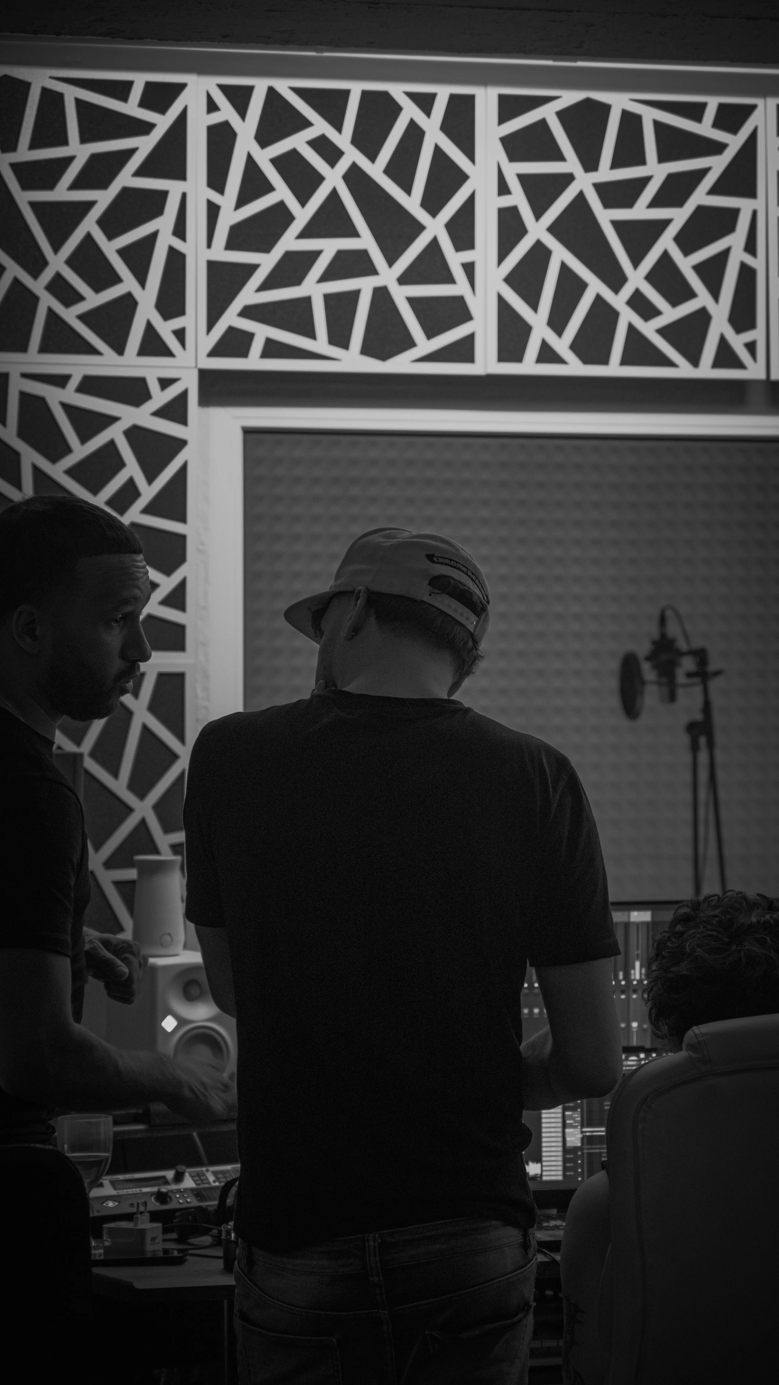 Studio d'enregistrement avec plusieurs personnes travaillant sur un ordinateur avec équipements audio, murs insonorisés et décor géométrique blanc et noir