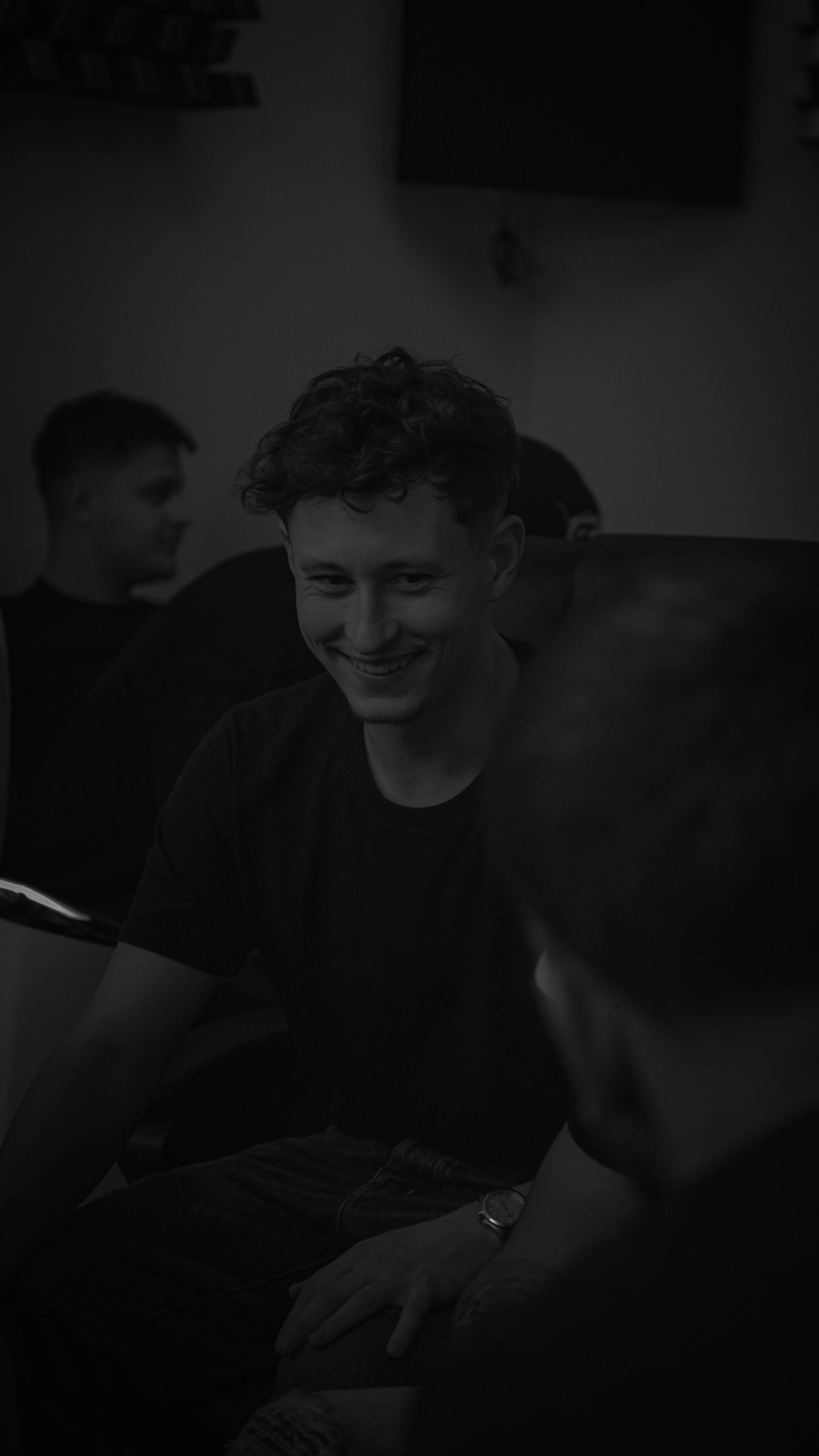 Jeune homme souriant, assis en groupe, dont d'autres personnes visibles en arrière-plan.