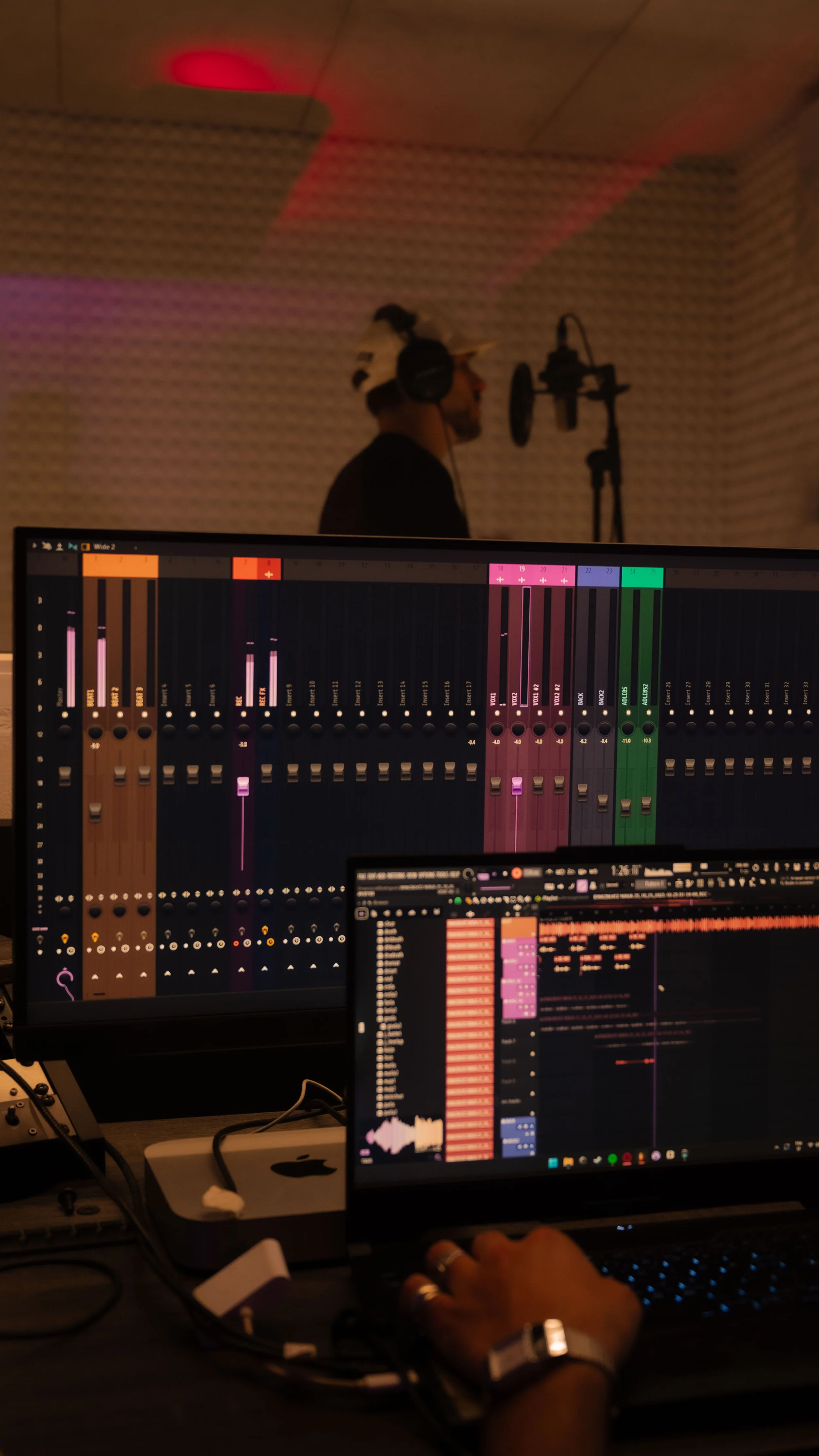 Studio d'enregistrement avec un homme au casque et un ordinateur affichant un logiciel de production musicale.