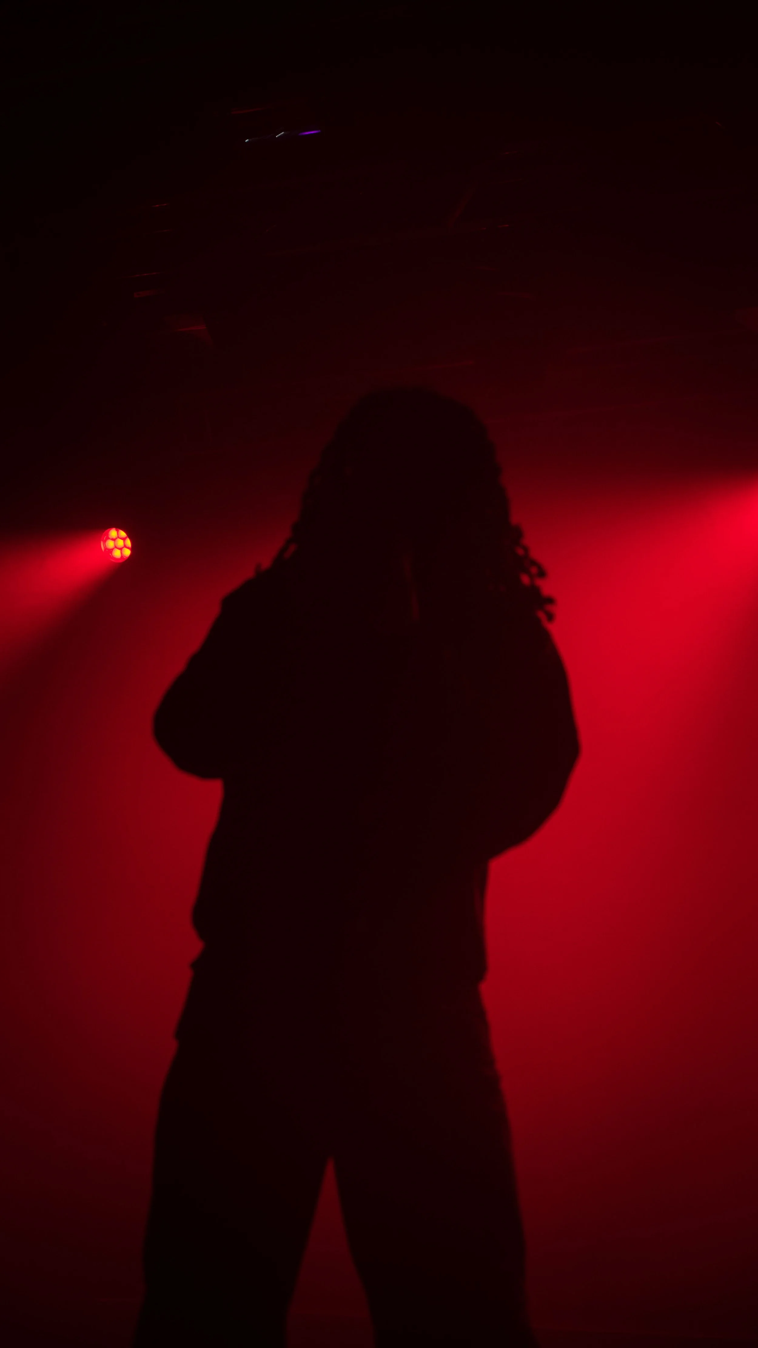 Silhouette d'une personne avec des lumières rouges et violettes dans un environnement sombre.
