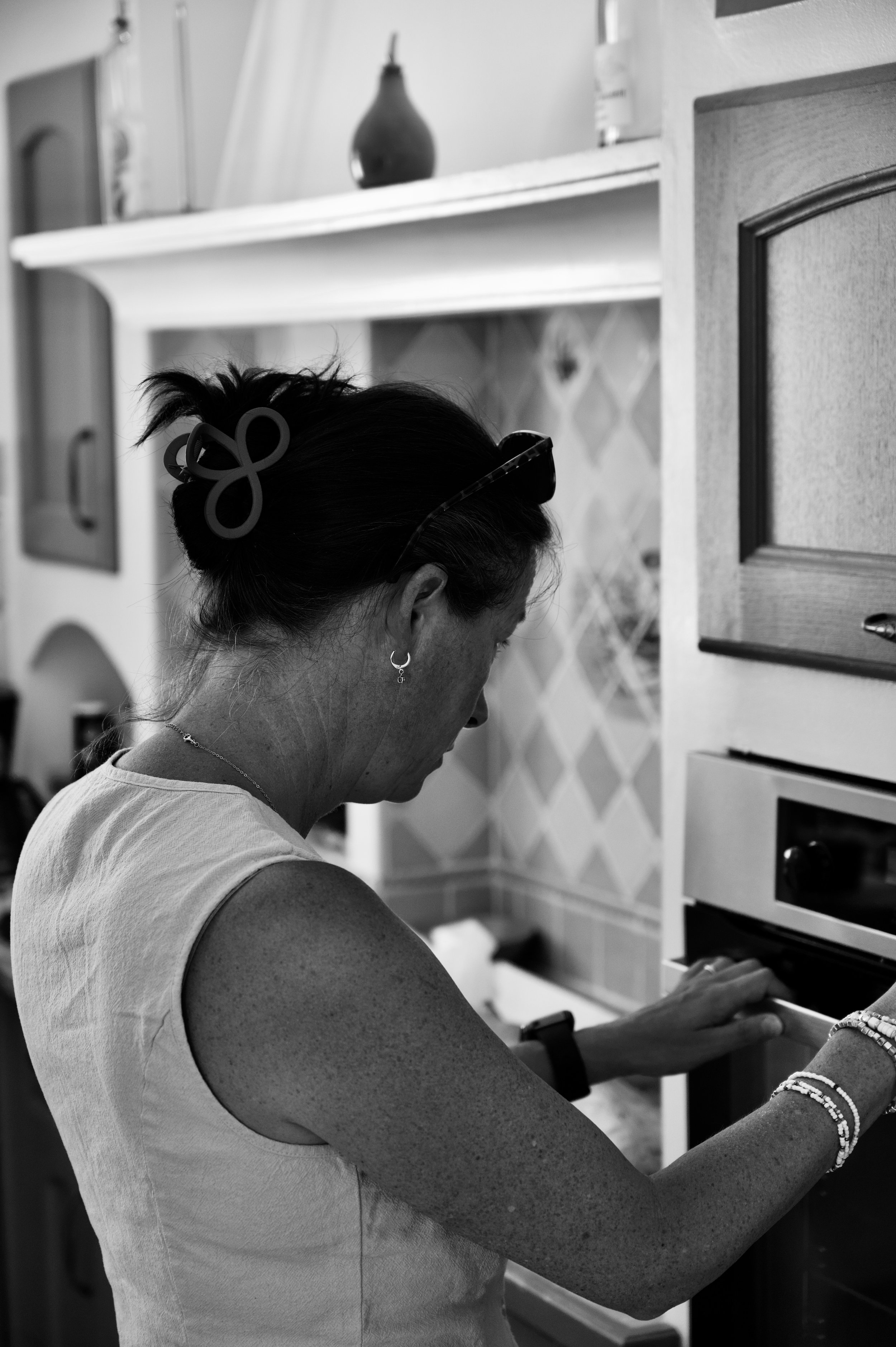 Une femme portant un haut sans manches, regarde dans une armoire ou un meuble, portant des bracelets et un collier, avec des cheveux attachés par un accessoire en forme de nœud.