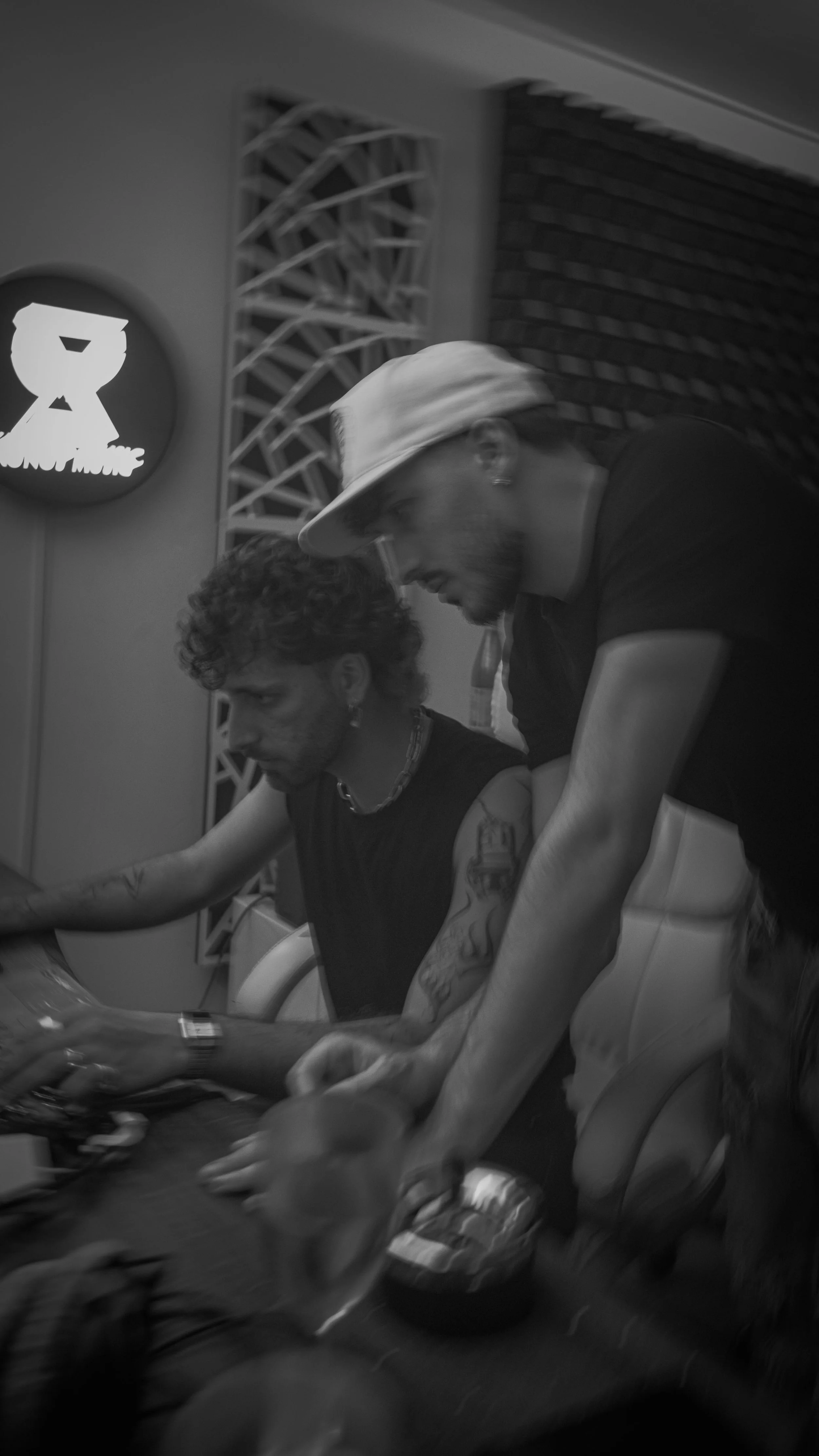 Deux hommes en train de jouer à un jeu de cartes dans une salle, un avec un chapeau blanc et l'autre avec des tatouages visibles, en noir et blanc.