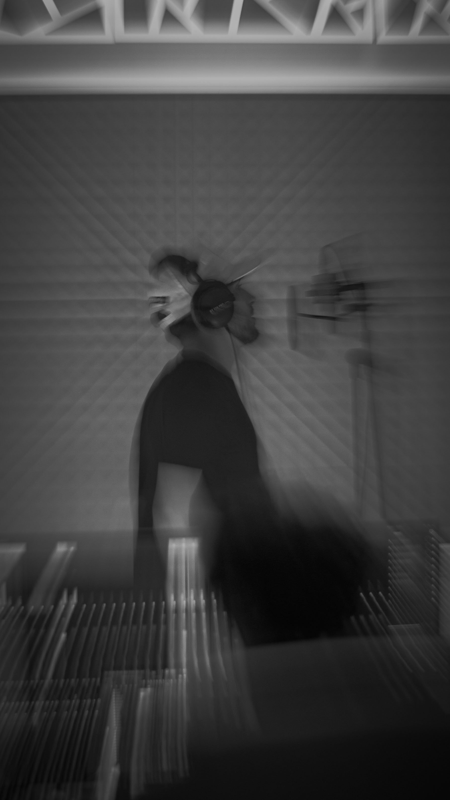 Photo en noir et blanc vue d'en haut d'une personne avec une casquette, vêtue d'un t-shirt à manches longues, marchant sur un escalator.