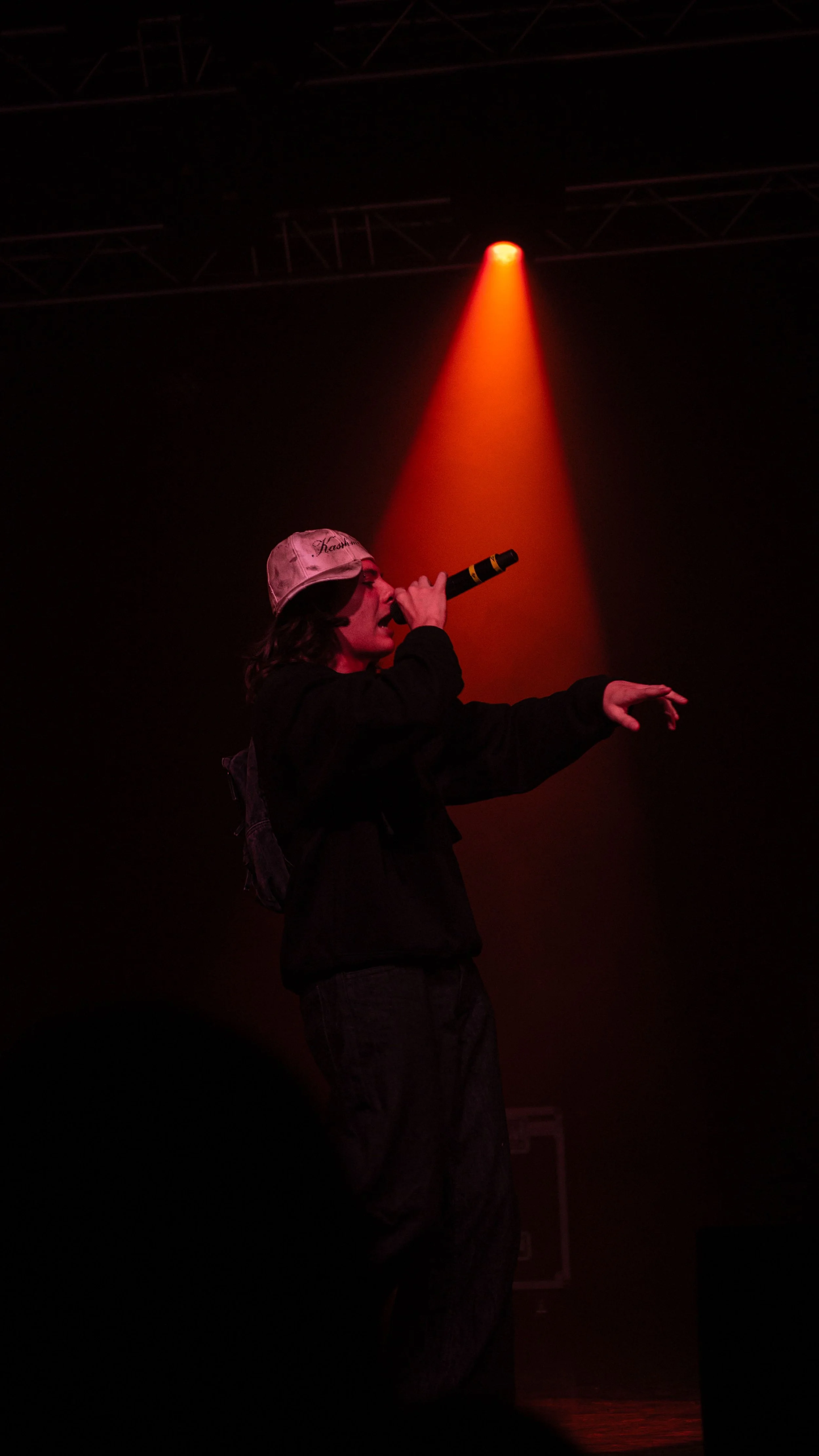 Un artiste de rap en train de chanter sur scène, portant une casquette blanche, sous un éclairage rouge.
