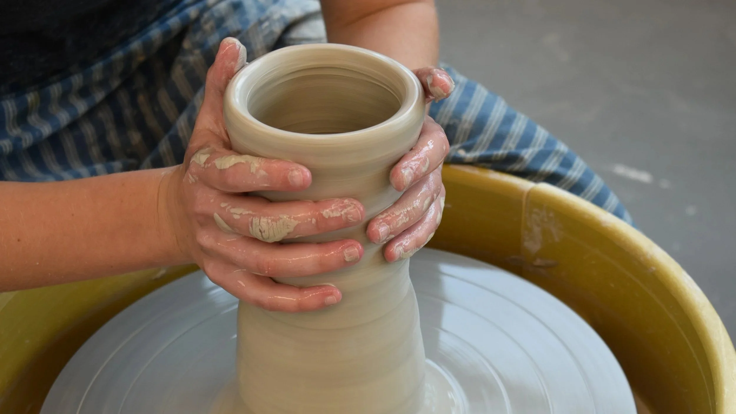Hands collaring a tall cylinder on the pottery wheel.