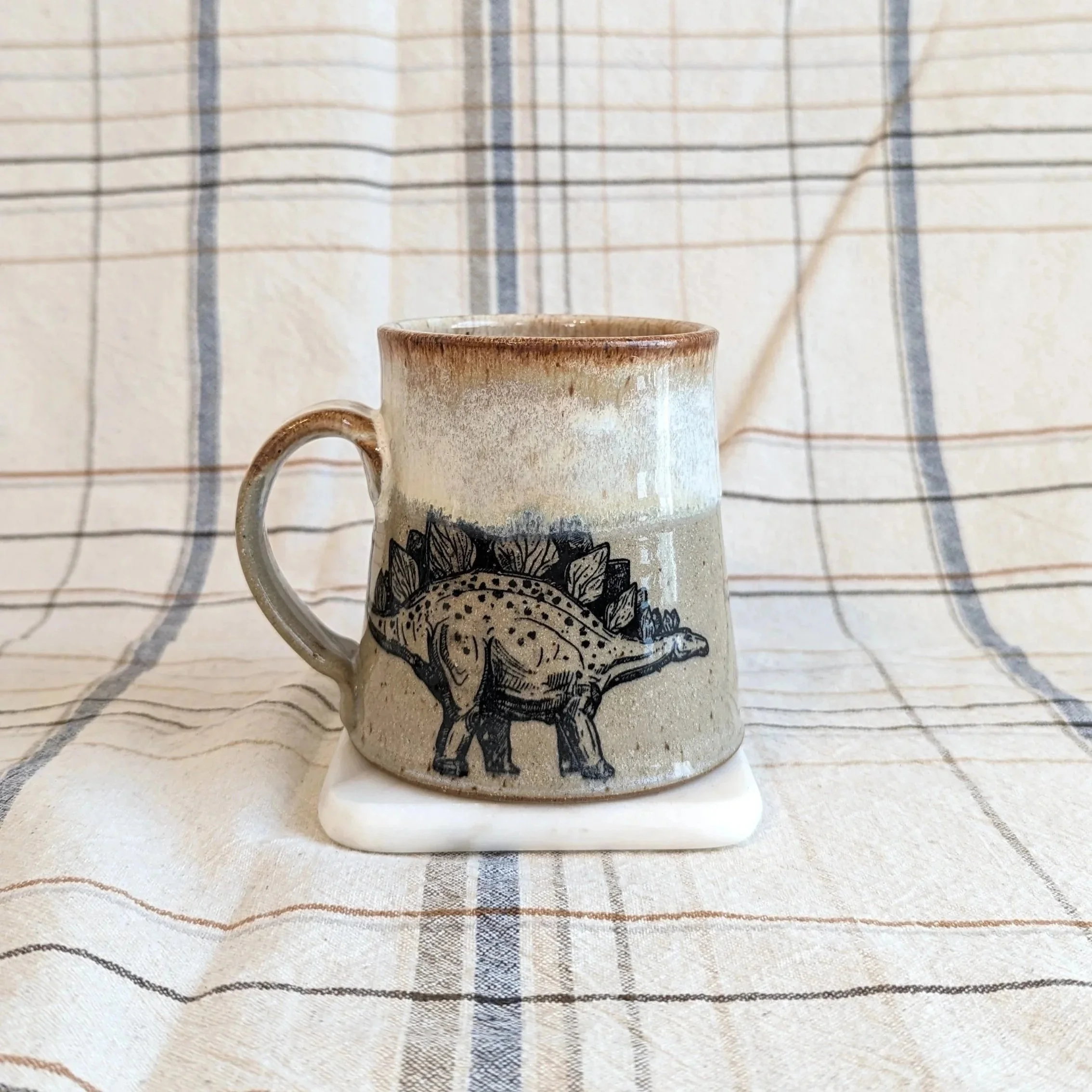 Light grey pottery mug with dinosaur decal.