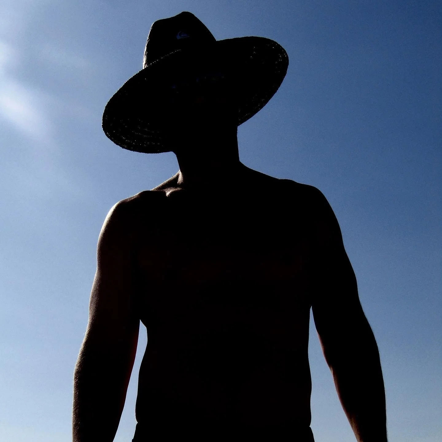 Silhouette of a person wearing a wide-brimmed hat against a blue sky.
