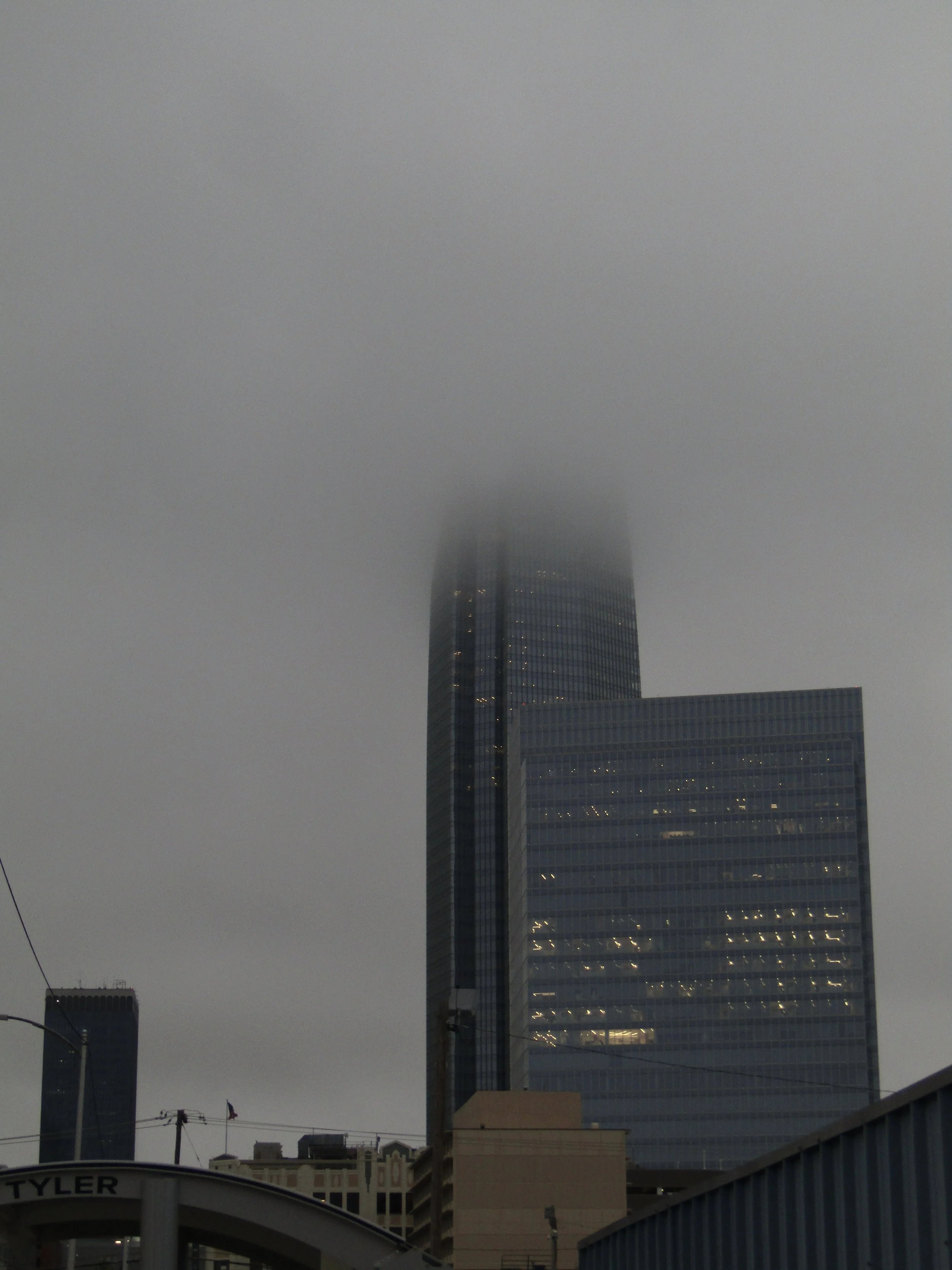 A tall skyscraper partially obscured by fog in an urban area.
