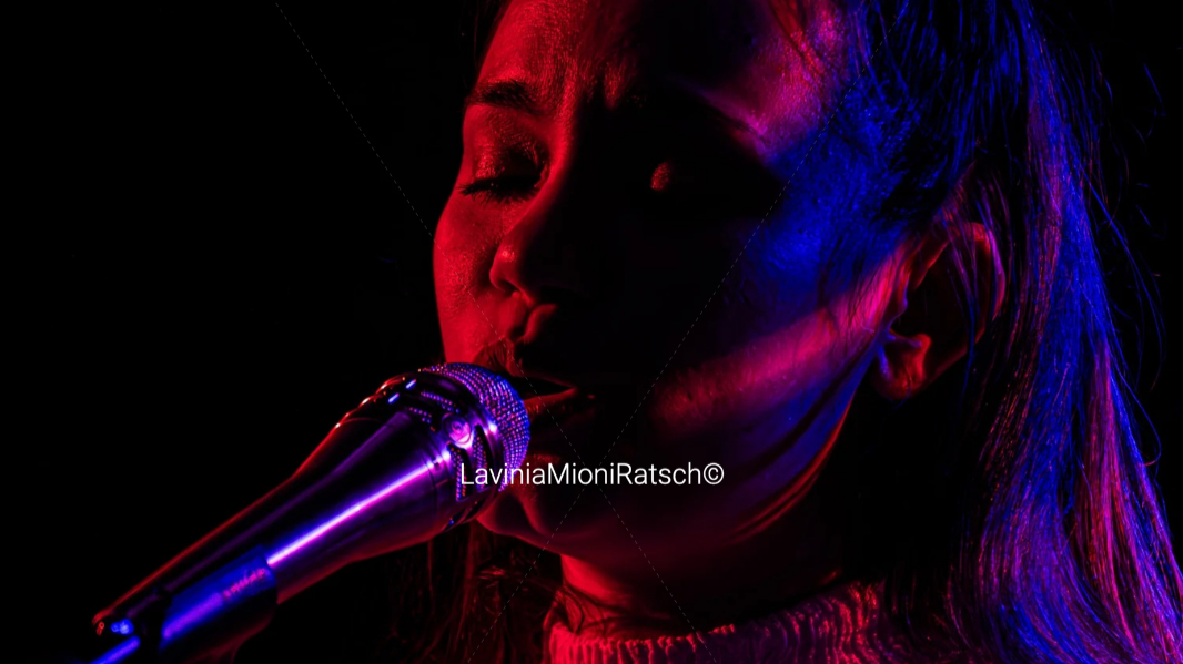 A woman singing into a microphone under colorful stage lighting.
