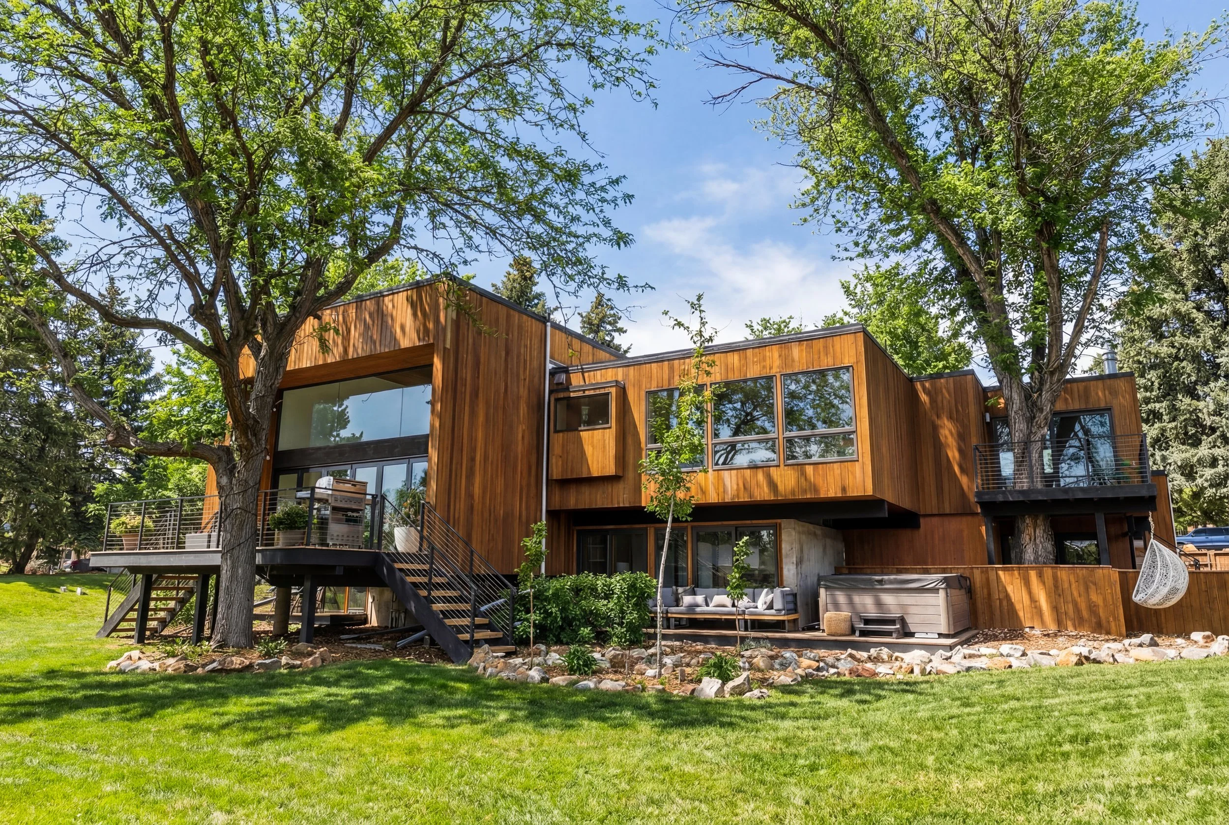 Modern wood-clad home in a Denver neighborhood with large windows, outdoor deck, and landscaped yard.