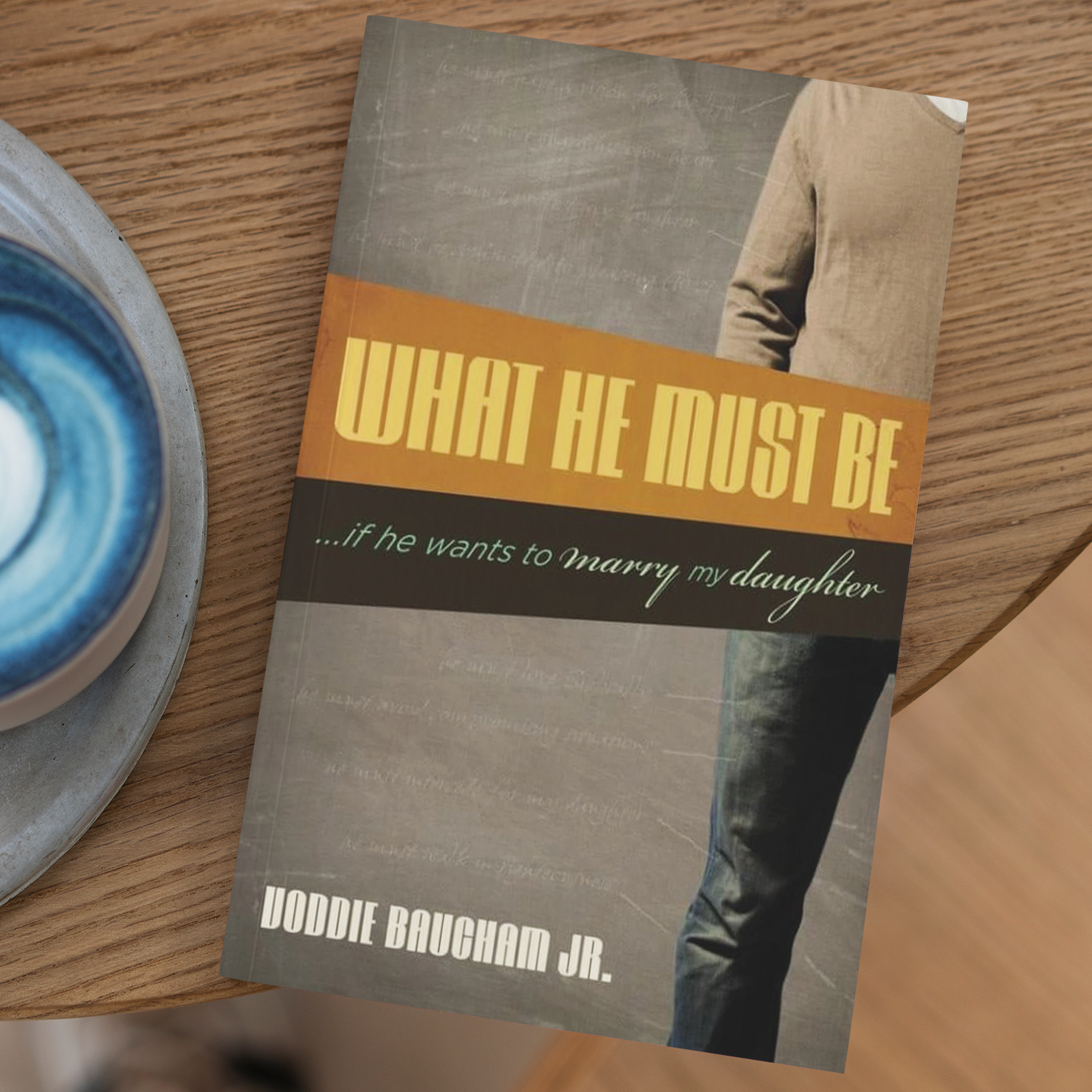 Book titled "What He Must Be... if he wants to marry my daughter" by Joddie Baugham Jr., placed on a wooden surface next to a ceramic bowl with a blue and white swirl design.