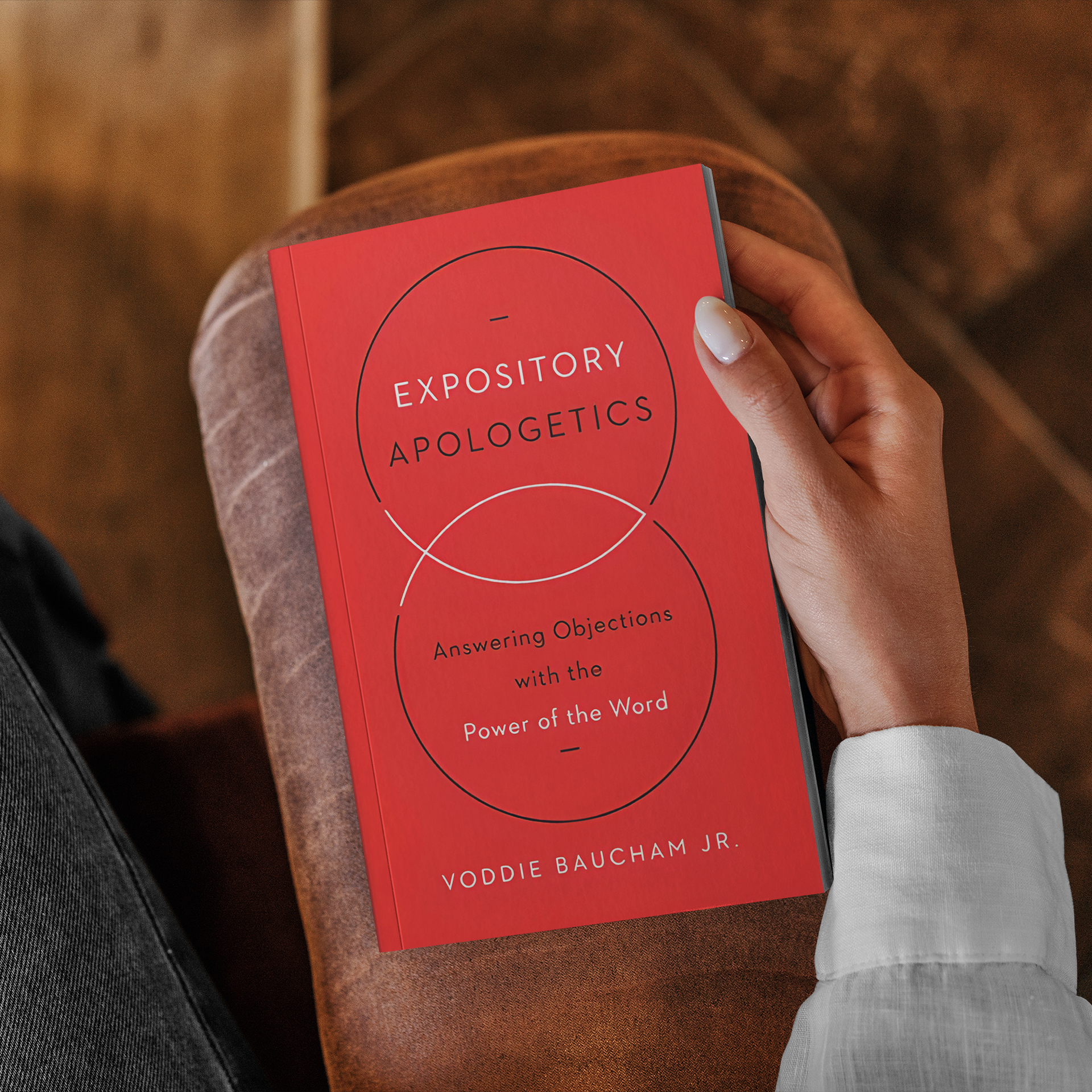 Person holding a red book titled 'Expository Apologetics' by Voddie Baucham Jr., with the subtitle 'Answering Objections with the Power of the Word'.