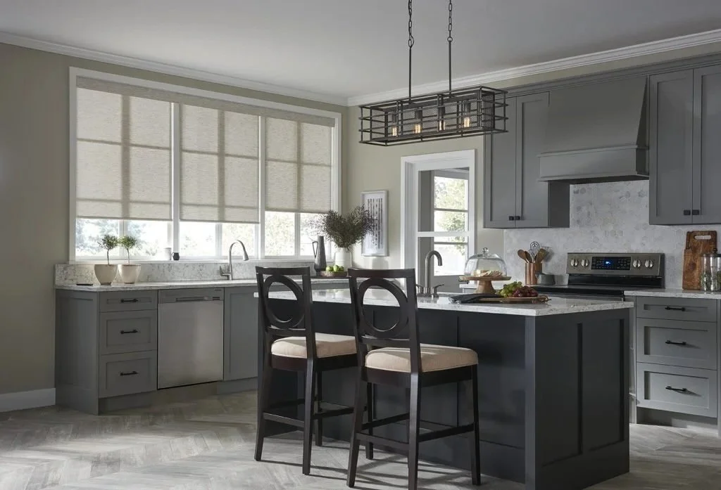 Modern kitchen with gray cabinets, a kitchen island, two bar stools, pendant light, and large window with blinds.