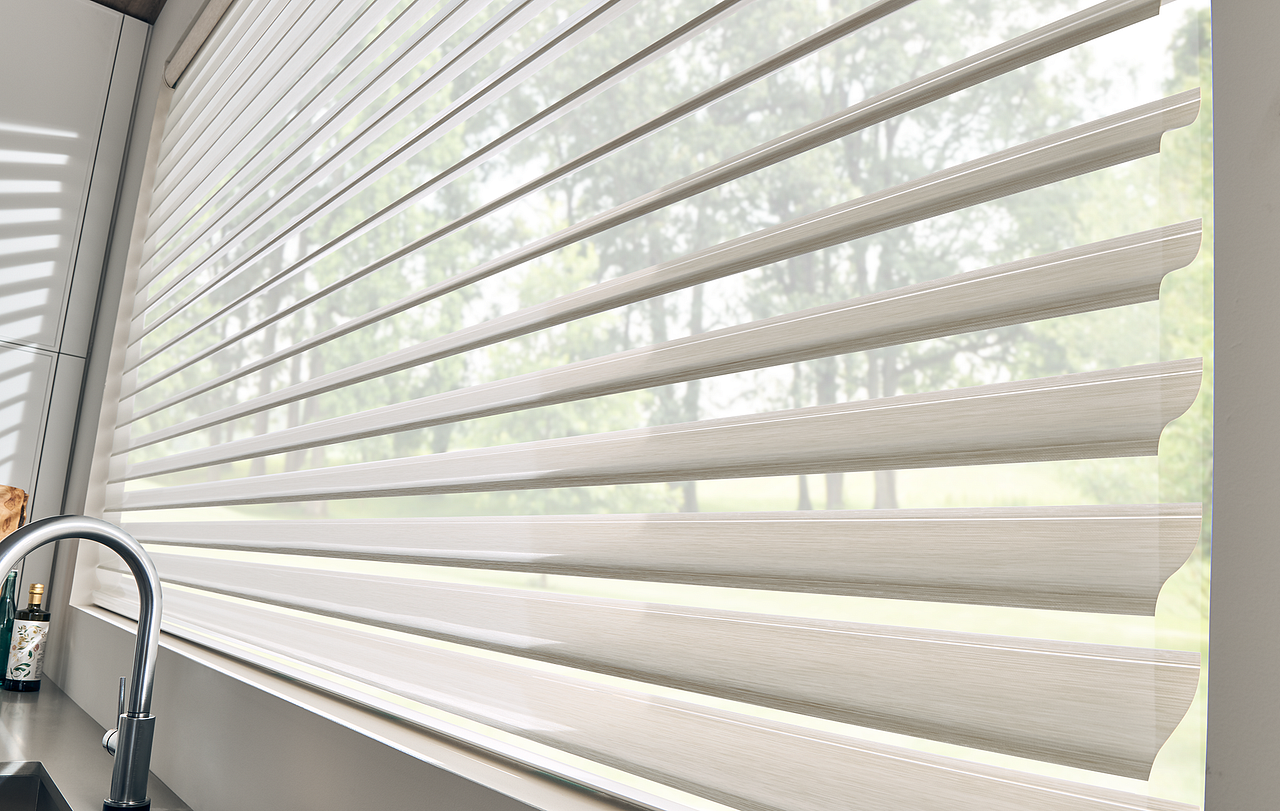 Close-up of a kitchen window with white horizontal blinds partially open, revealing greenery outside.
