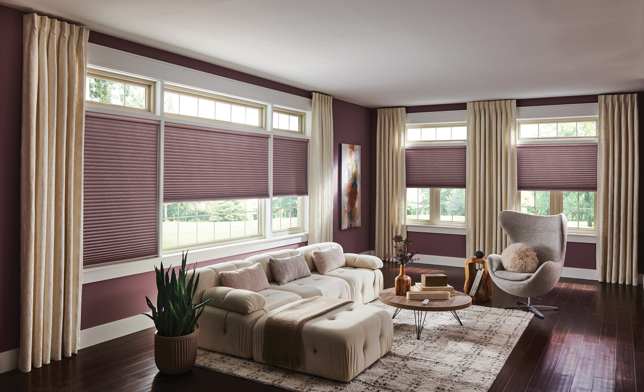 Living room with large windows, purple walls, beige curtains, white sofa, gray armchair, wooden coffee table, and decorative accents.