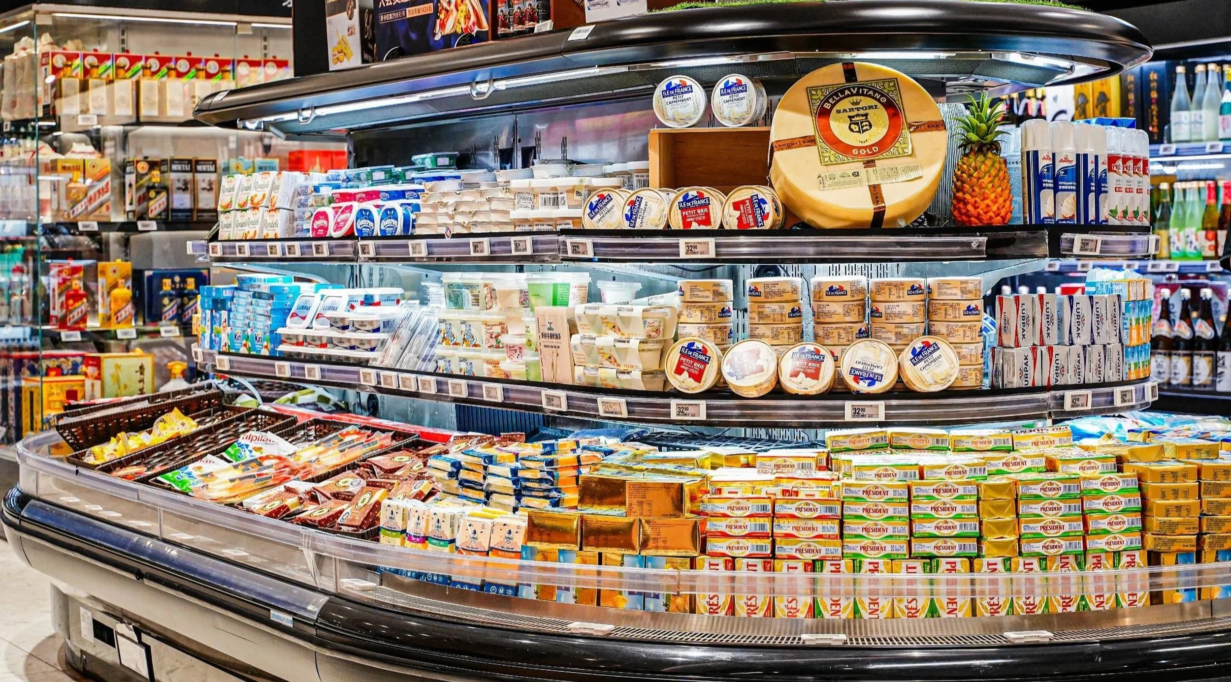 Display of various dairy products on store shelves, including cheese, butter, and margarine, with a pineapple on the top shelf.