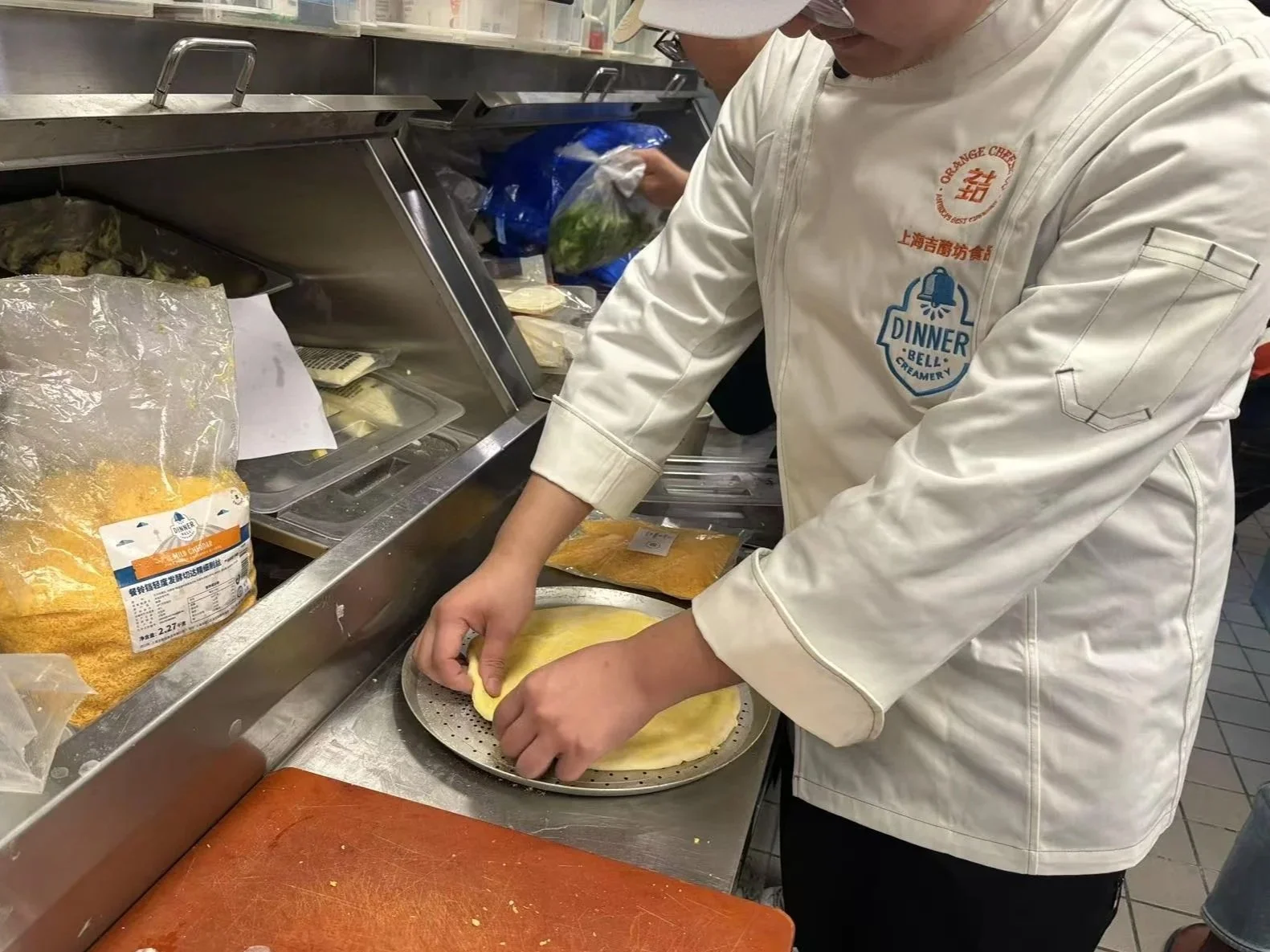 A chef in a white apron preparing food in a commercial kitchen, with various ingredients and packaging around him.