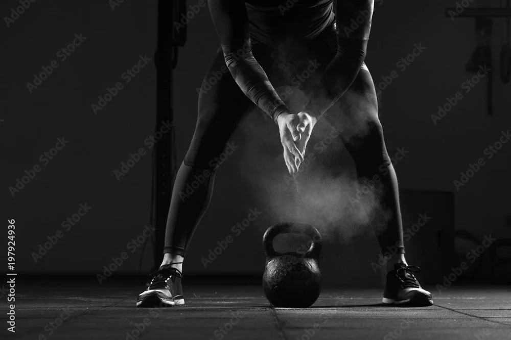A man in sportswear is preparing to lift a kettlebell during a workout in a gym, with visible steam rising from his exertion.