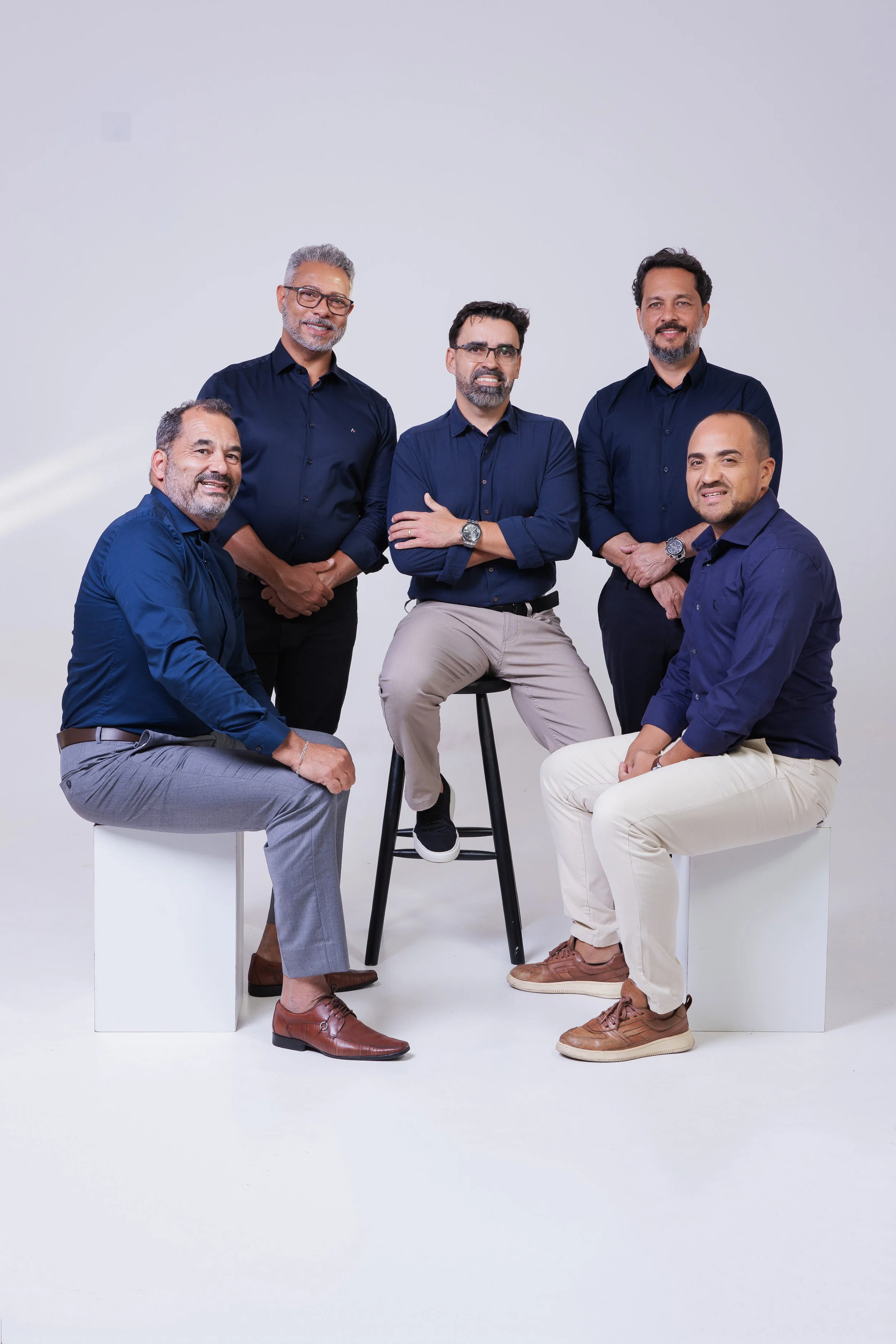 Seis homens sentados e de pé, vestidos de azul, posando em fundo branco.