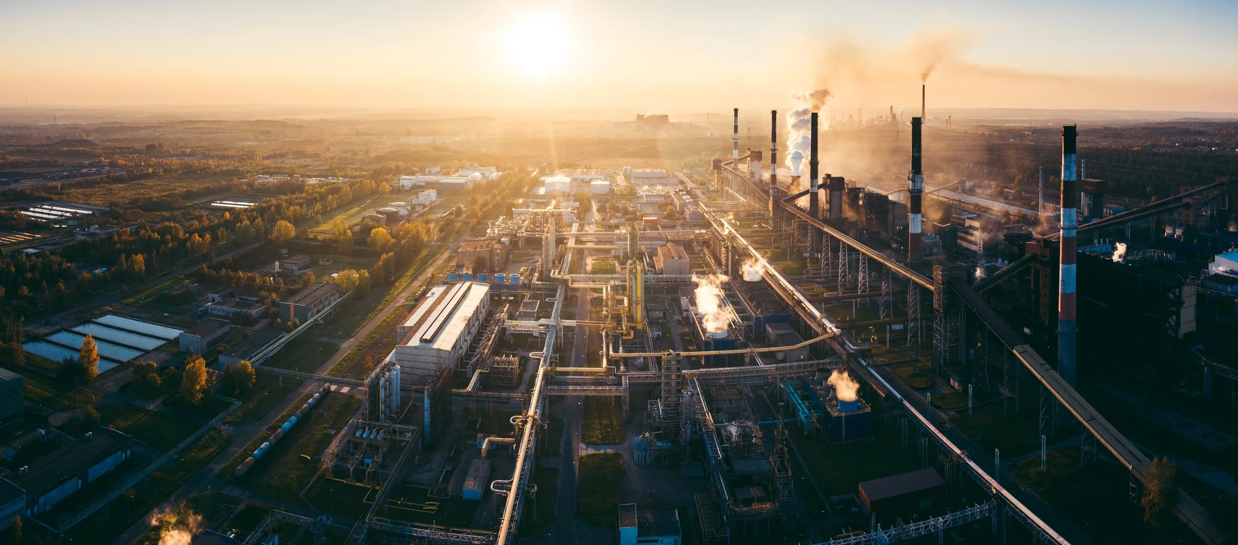 Planta industrial com várias chaminés emitindo fumaça ao pôr do sol