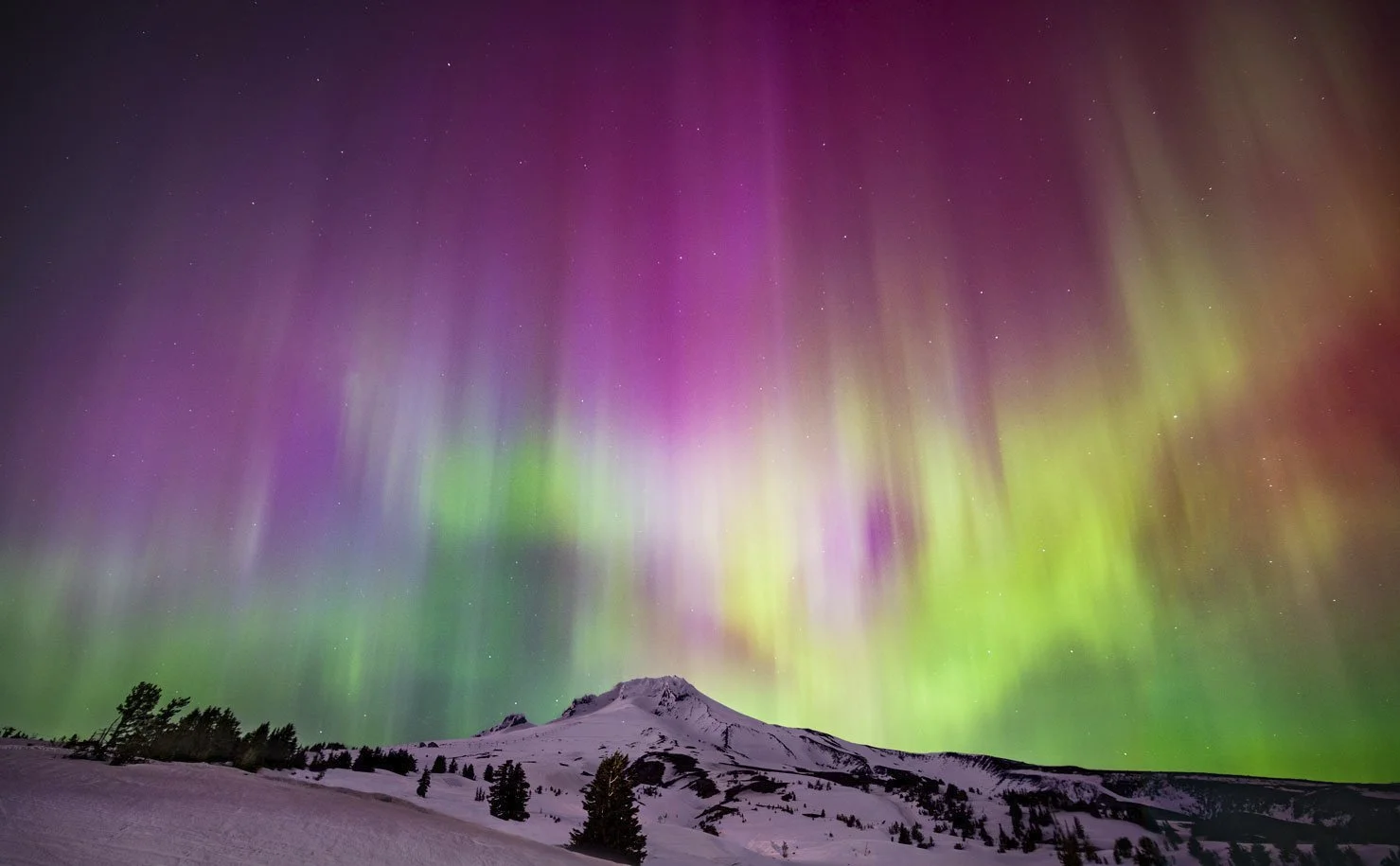 Northern lights over a snow-covered mountain landscape with trees at night.