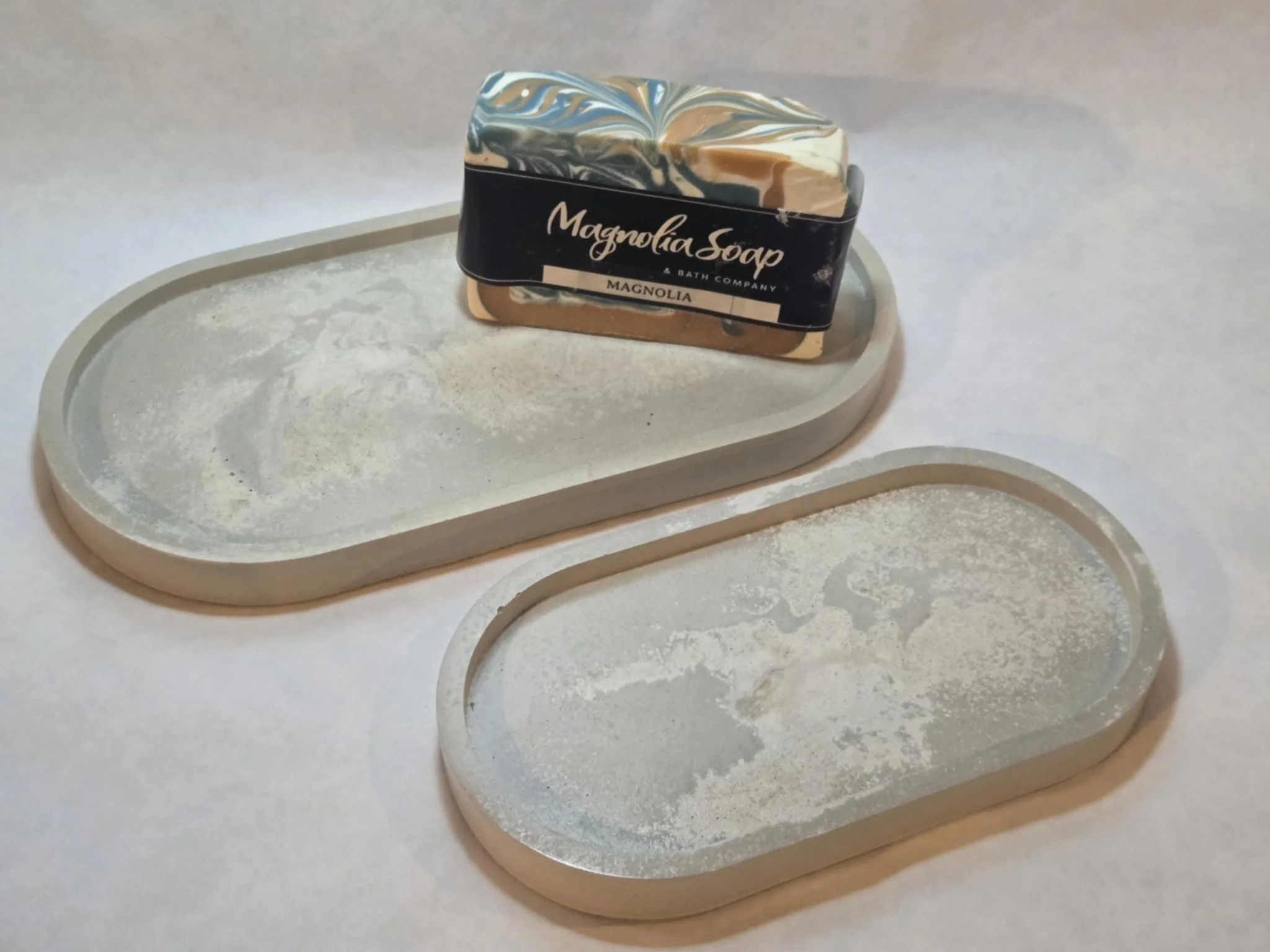 A marble-patterned bar of Magnolia Soap resting on two rectangular soap dishes with a dusting of powder.