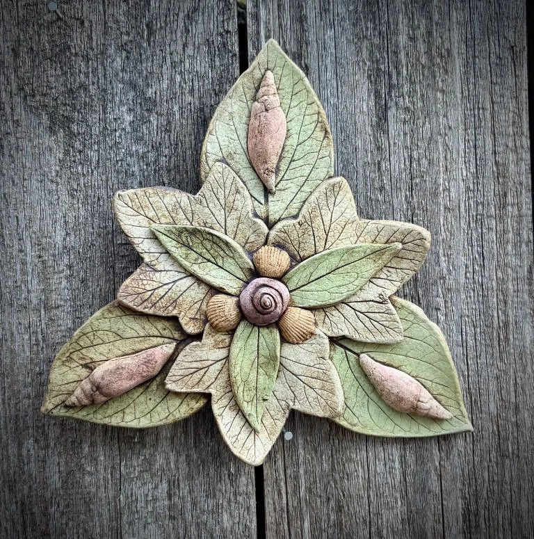 Decorative wall art resembling a cluster of leaves, acorns, and a snail shell, arranged on a wooden background.