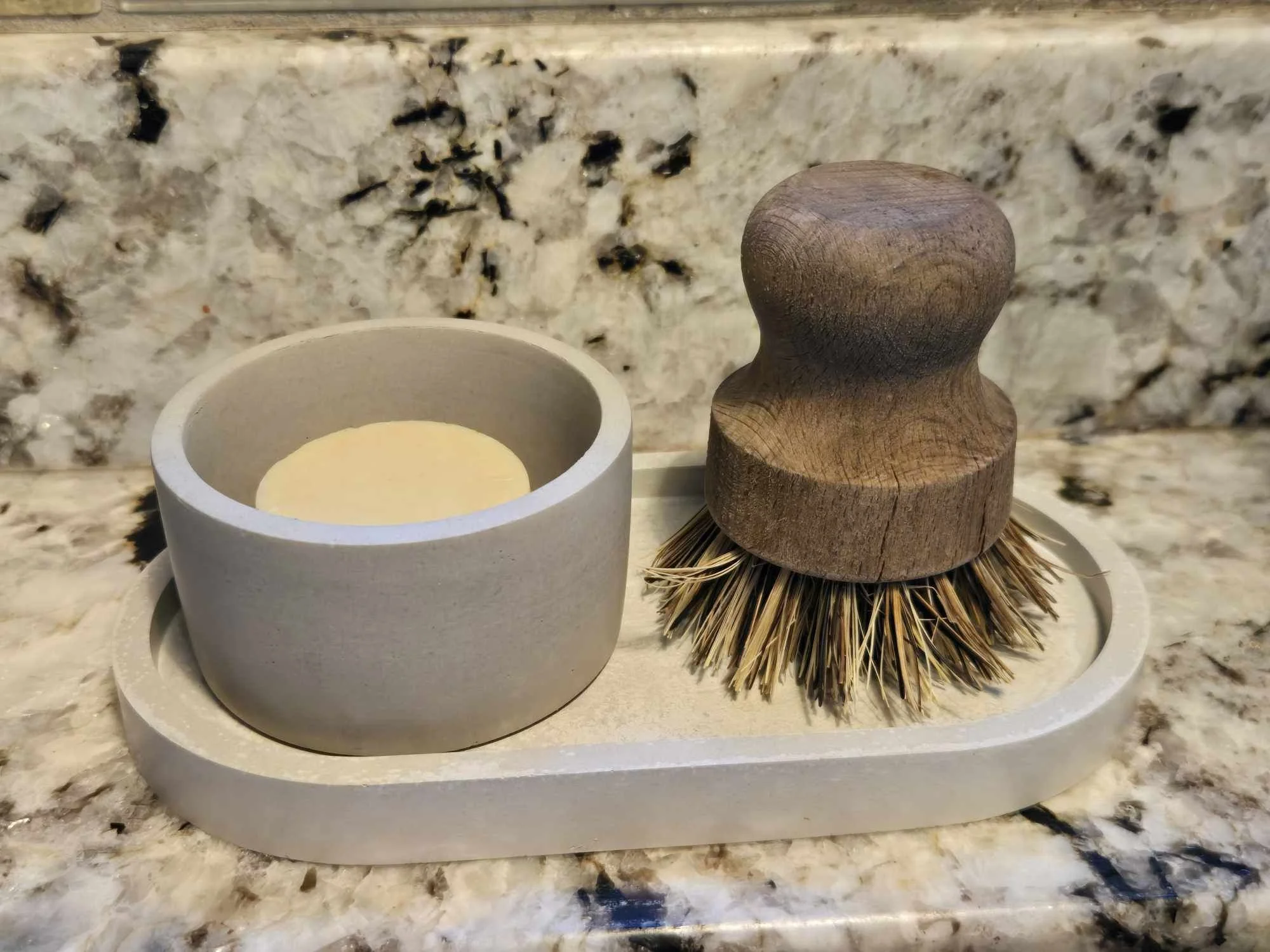 A candle and dish brush on a kitchen countertop with a marble pattern.