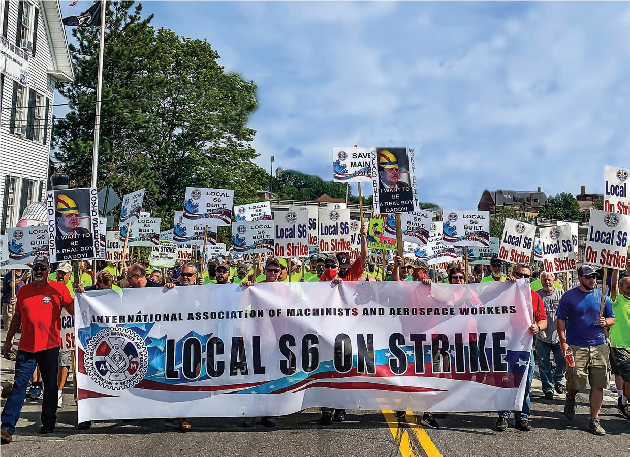 A large group of members from IAM Local S6 marching down a street tolding a large banner and picket signs that read "Local S6 on Strike"