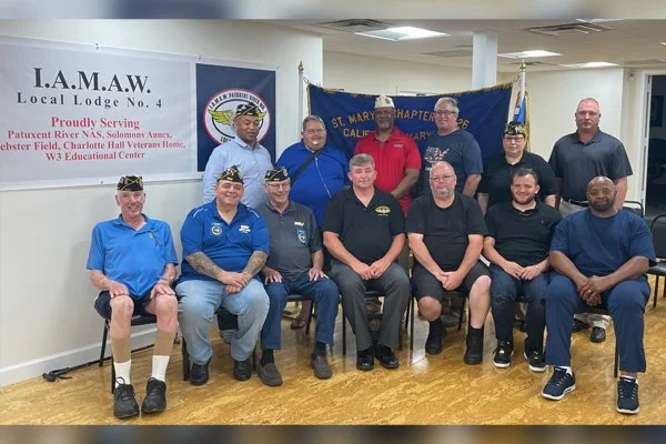 Group of eleven men sitting and standing in a room with banners for I.A.M.A.W. and California veterans organizations.